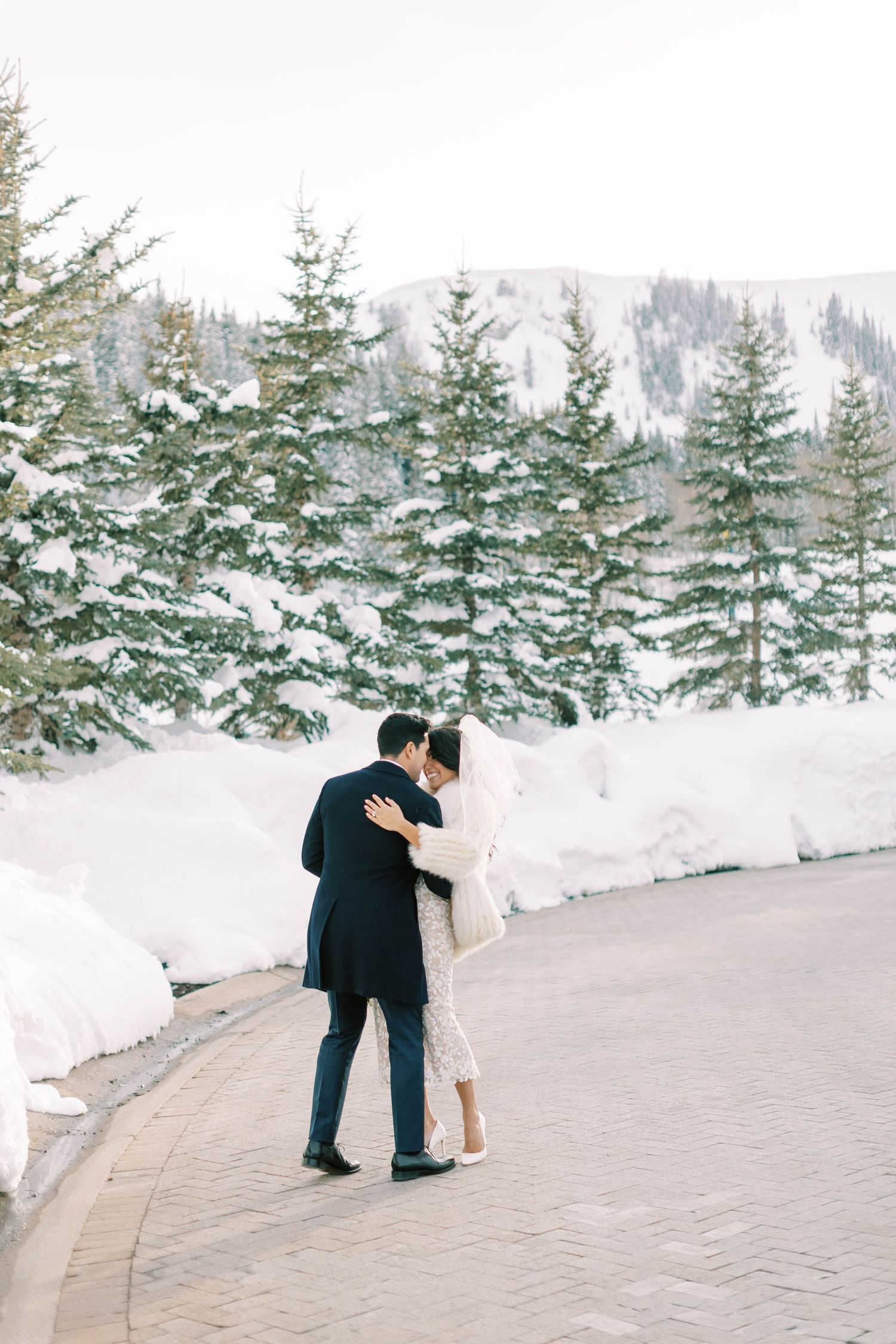 Couple embracing on mountain path with snow-covered pine trees in background at montage deer valley.