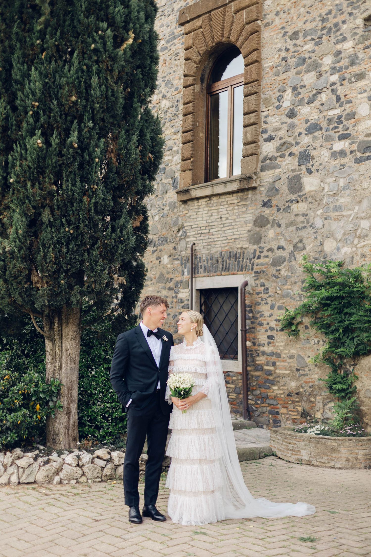 Newlyweds share intimate moment in front of rustic Italian villa entrance.