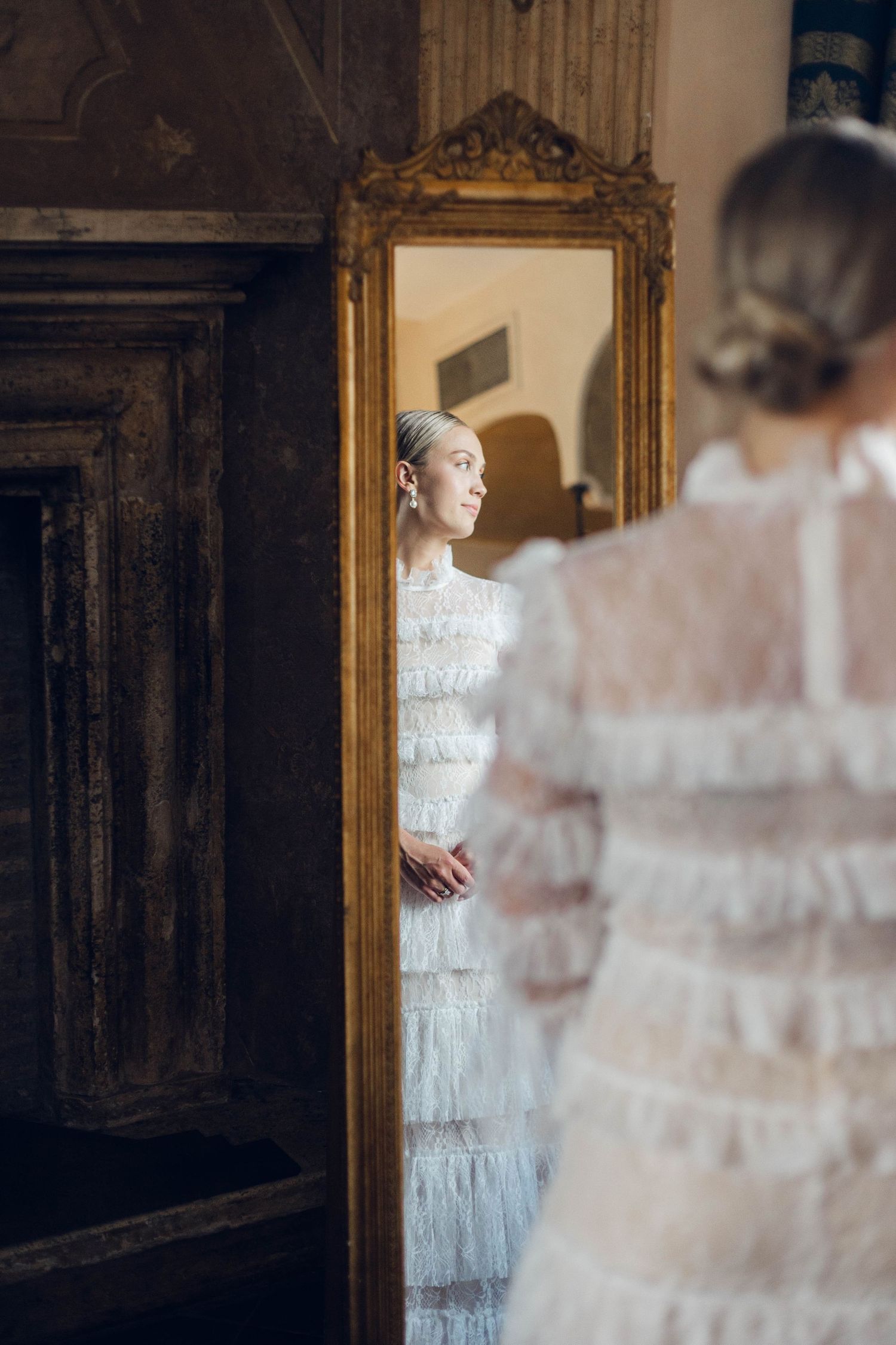White tiered lace dress reflected in an ornate gold-framed mirror.