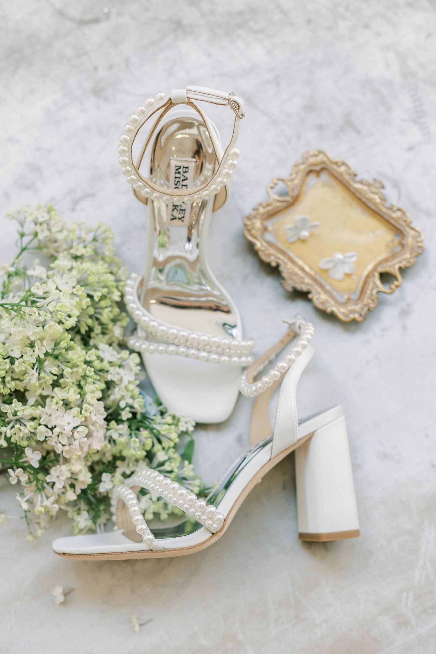 Pearl-embellished white bridal sandals with block heel next to delicate floral decor.