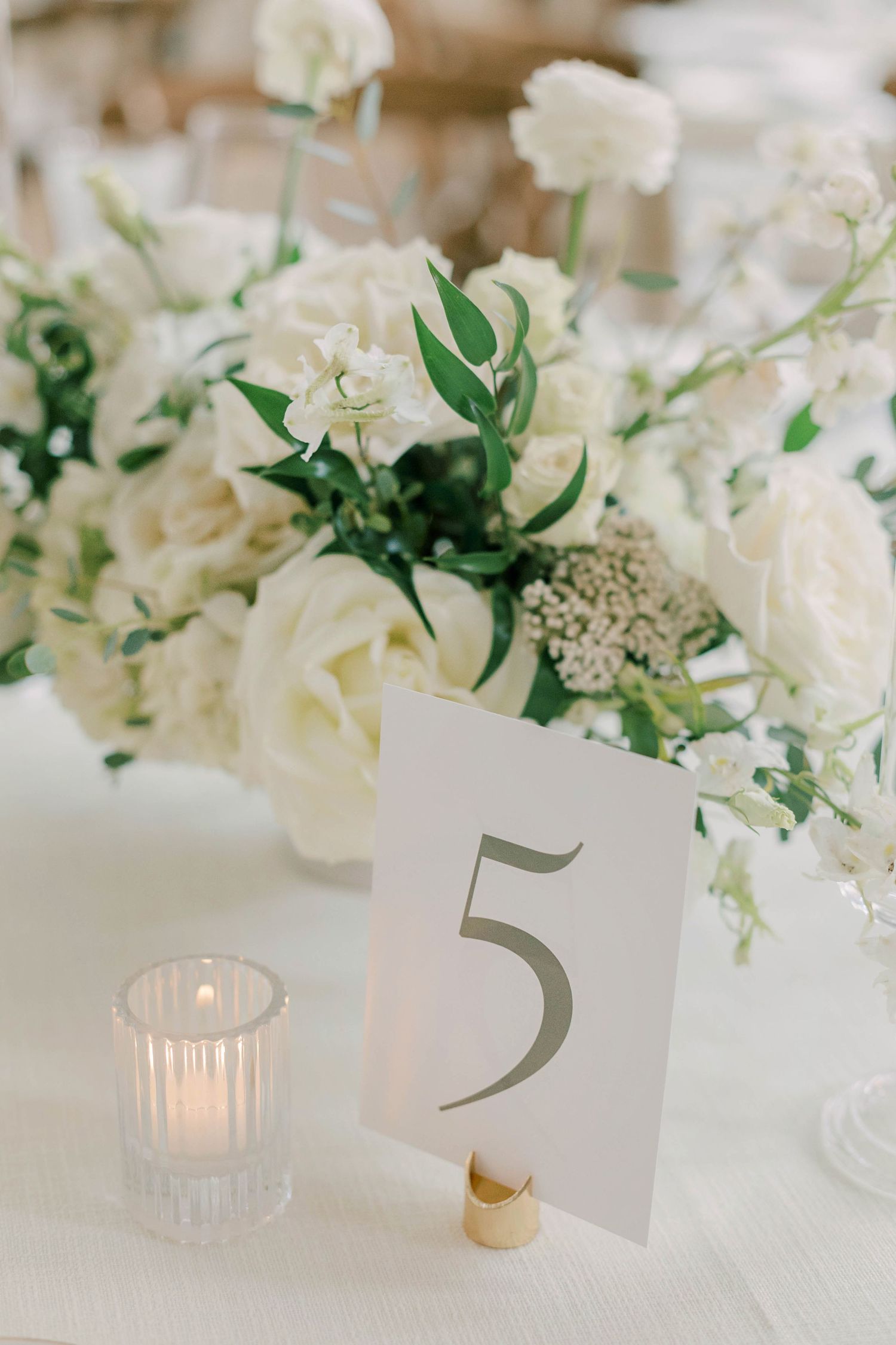 White rose centerpiece with table number 5 and votive candle on white linen.