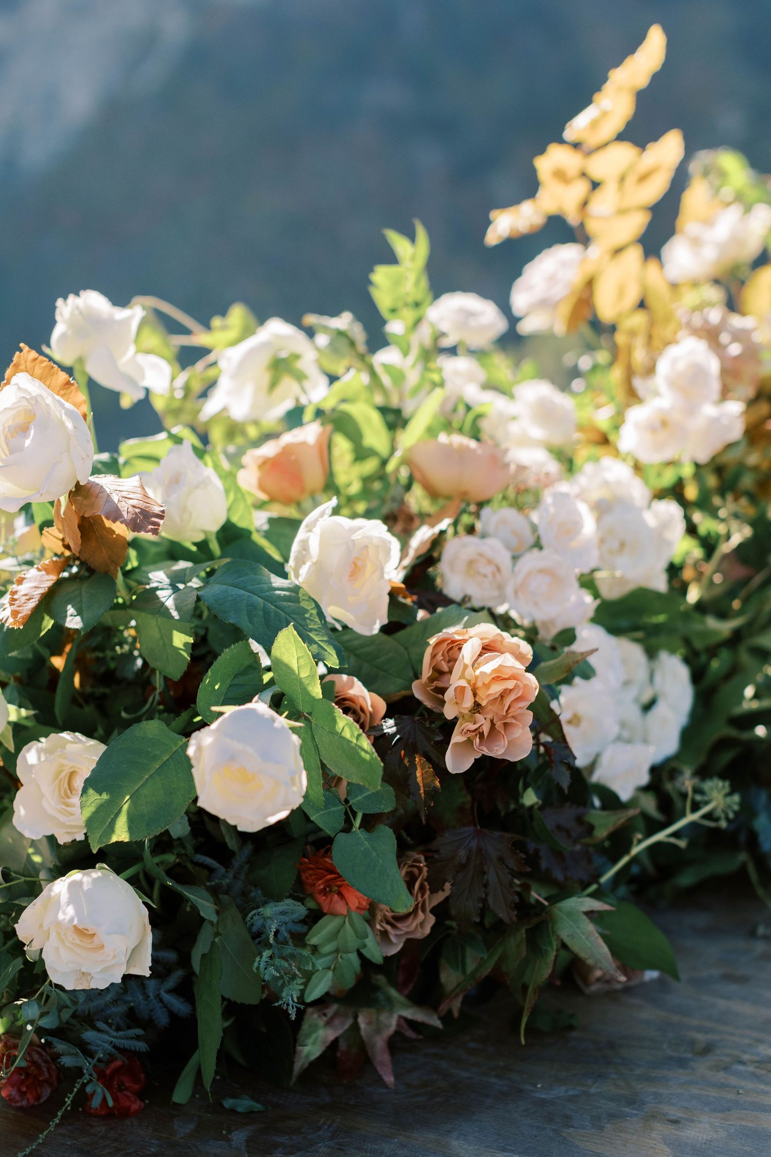 Elegant white roses and greenery floral arrangement against a mountain backdrop.