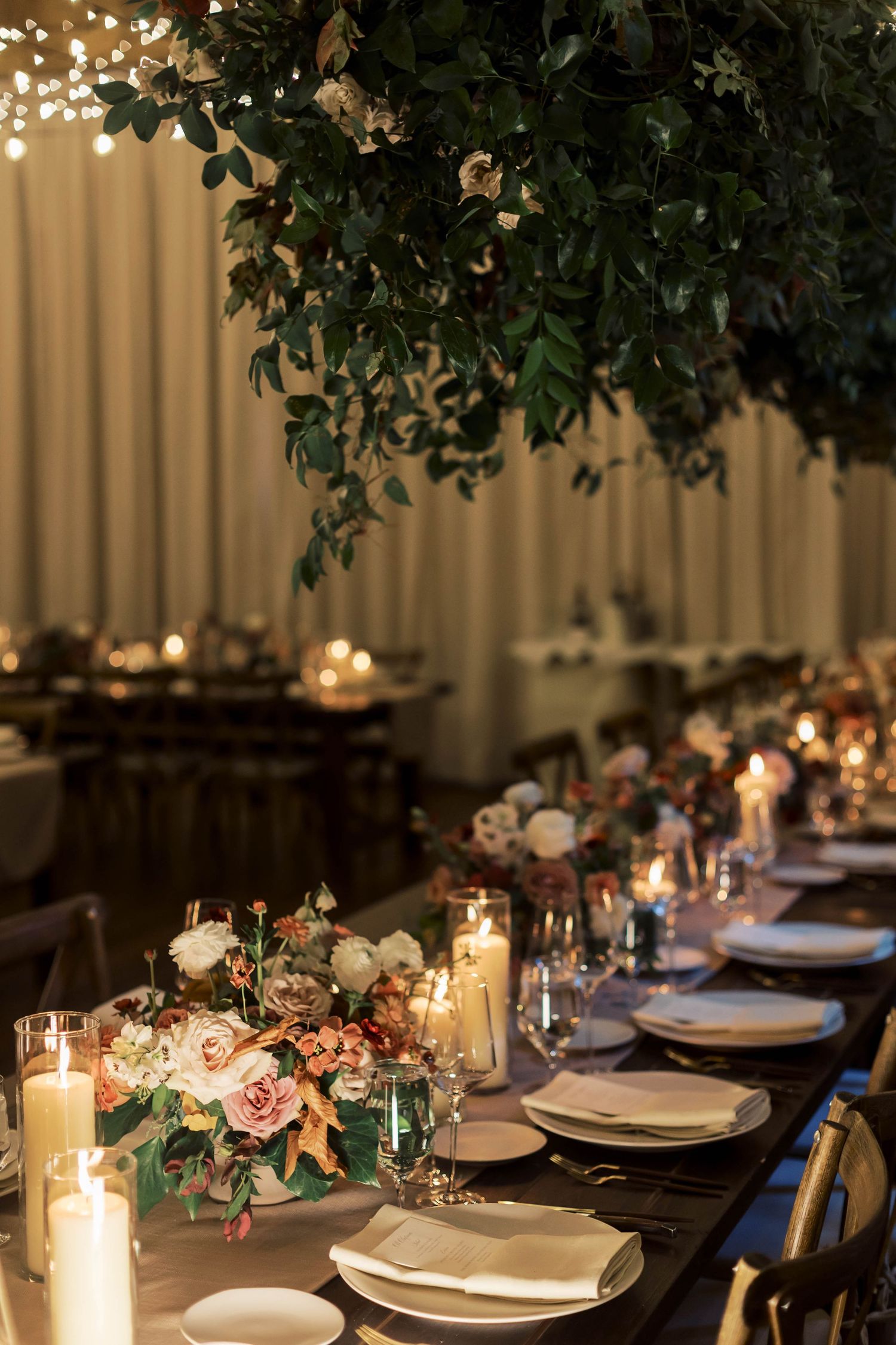 Elegant wedding reception table with hanging greenery, candles, and floral centerpieces.