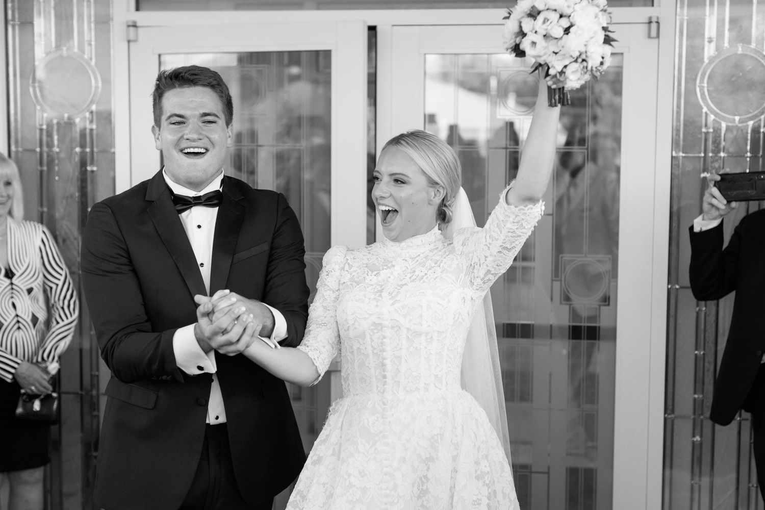 A joyous wedding exit moment with celebratory gestures and a bouquet held high.