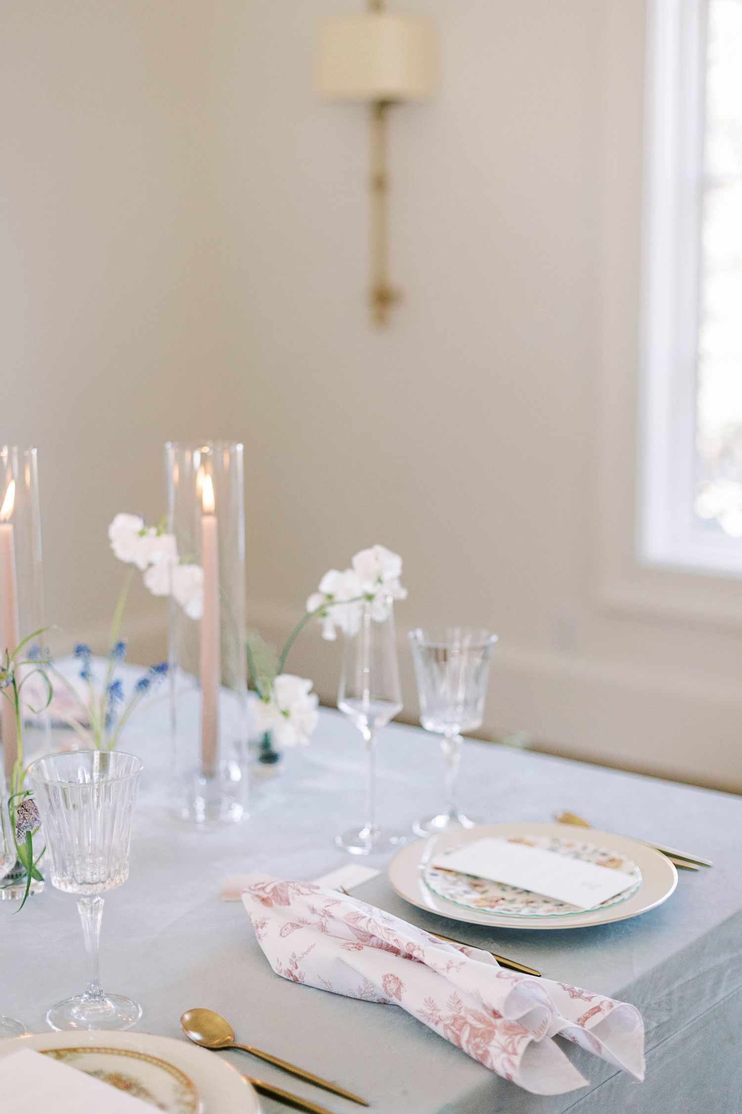 Romantic table setting with tall candles, white flowers, and soft blue linens.