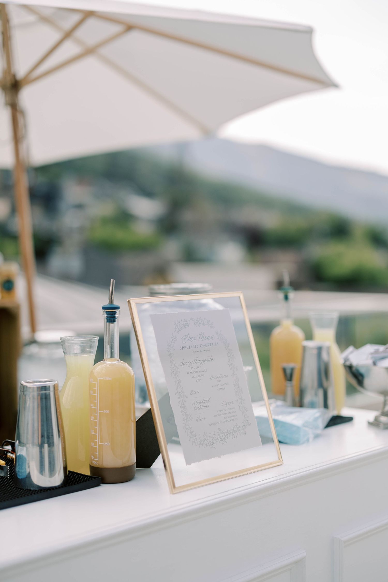 Wedding beverage station with menu and refreshments under white umbrella.