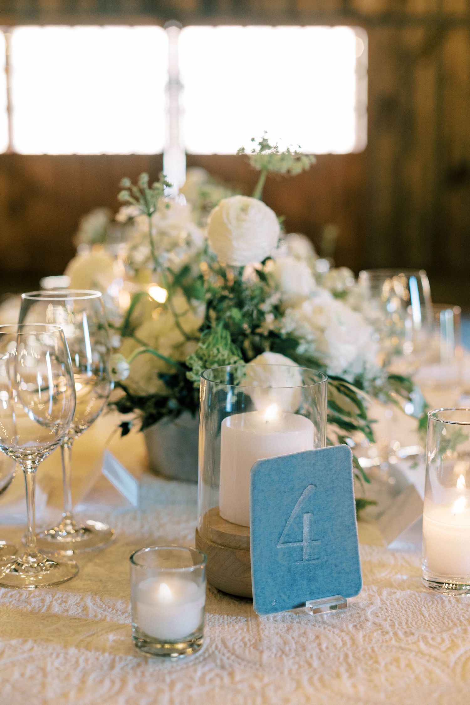 Wedding table decor with blue table number, white flowers, and glowing candles.
