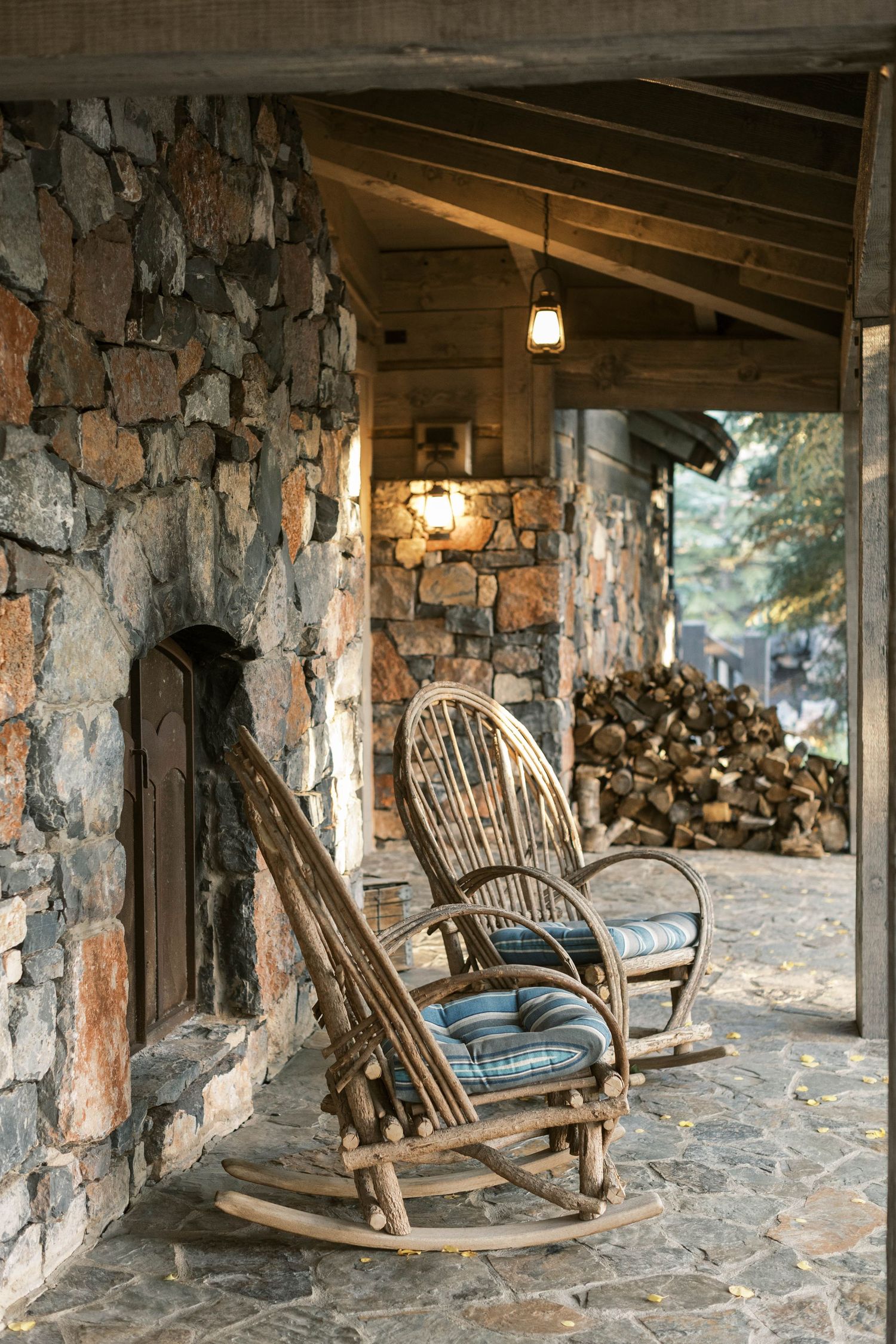 Rustic stone porch with wooden rocking chairs and stacked firewood.