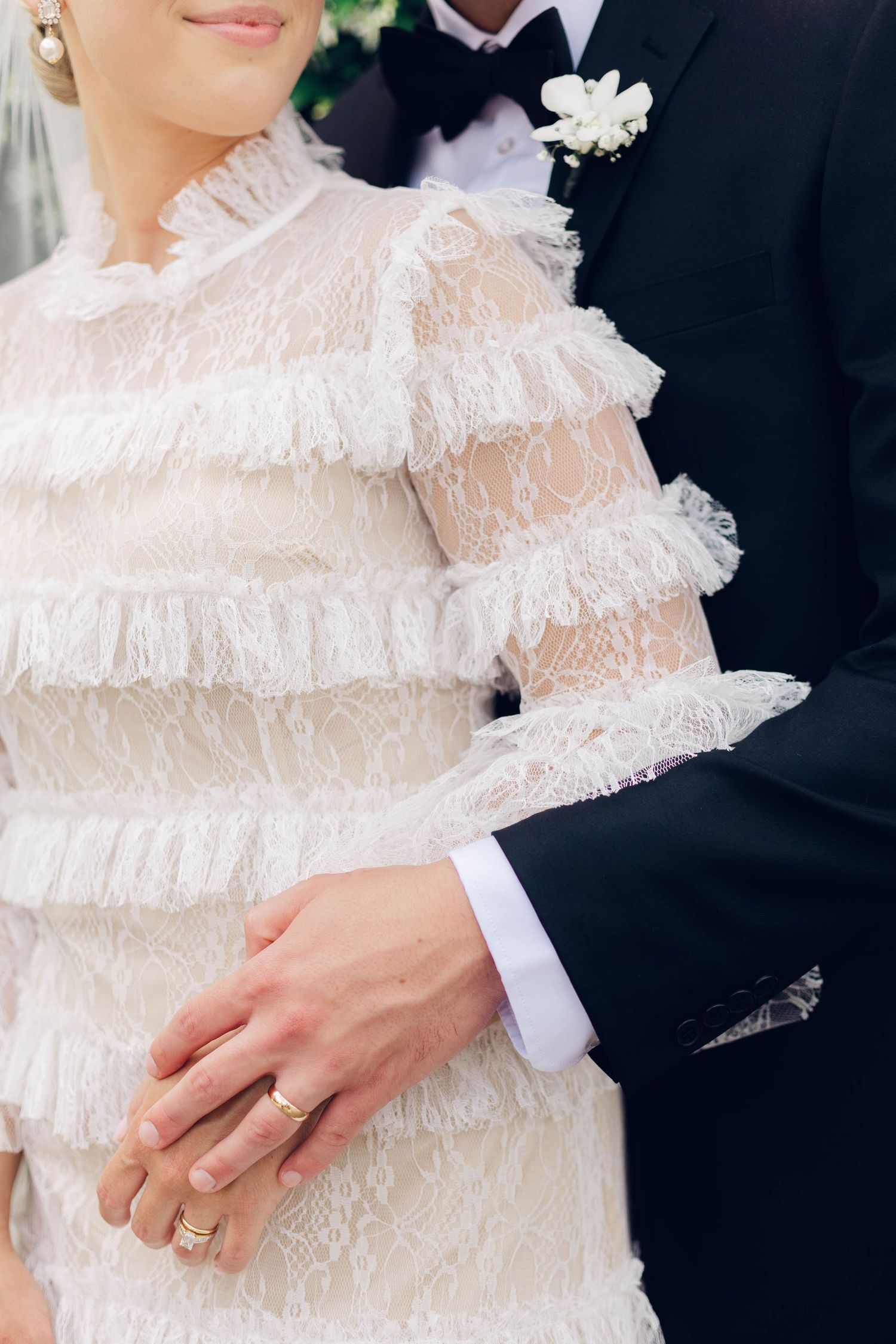 Close-up of couple's hands showing wedding rings and dress detail.