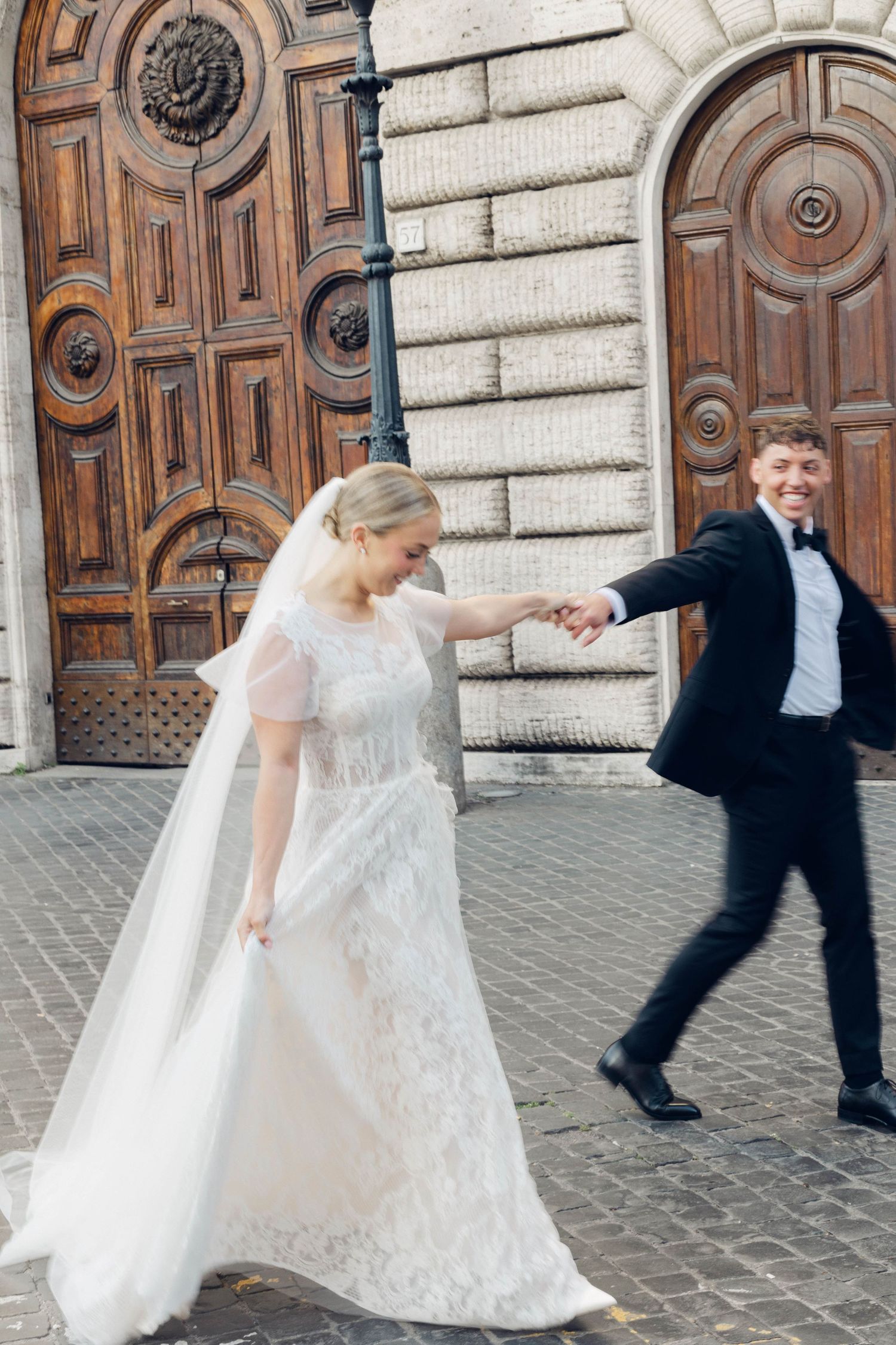 Playful wedding couple dancing outside ornate wooden doors of historic building of rome italy