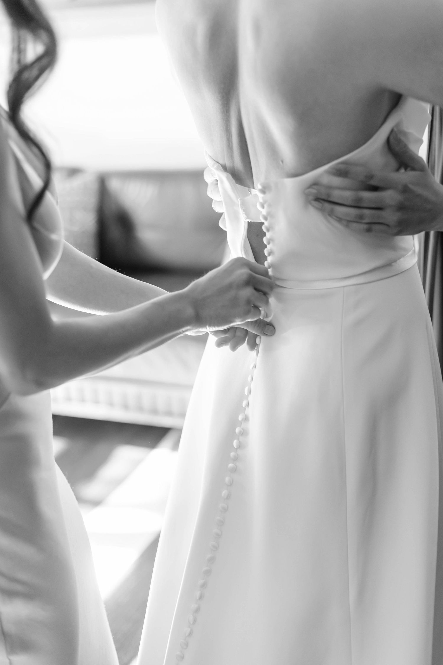 Close-up black and white photo of buttons being fastened on a white wedding dress.