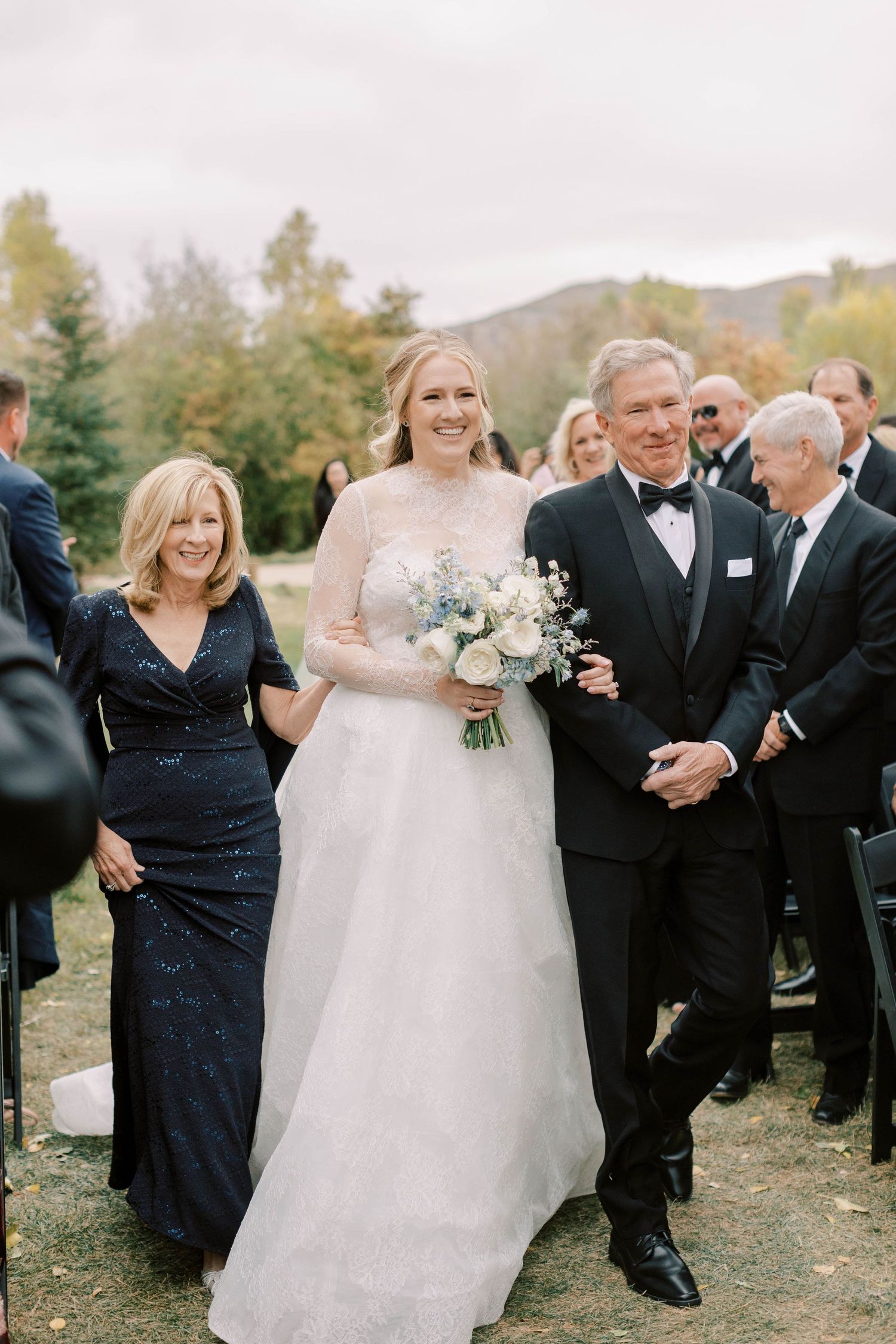 A joyful wedding processional moment captured outdoors with formal attire and autumn scenery.