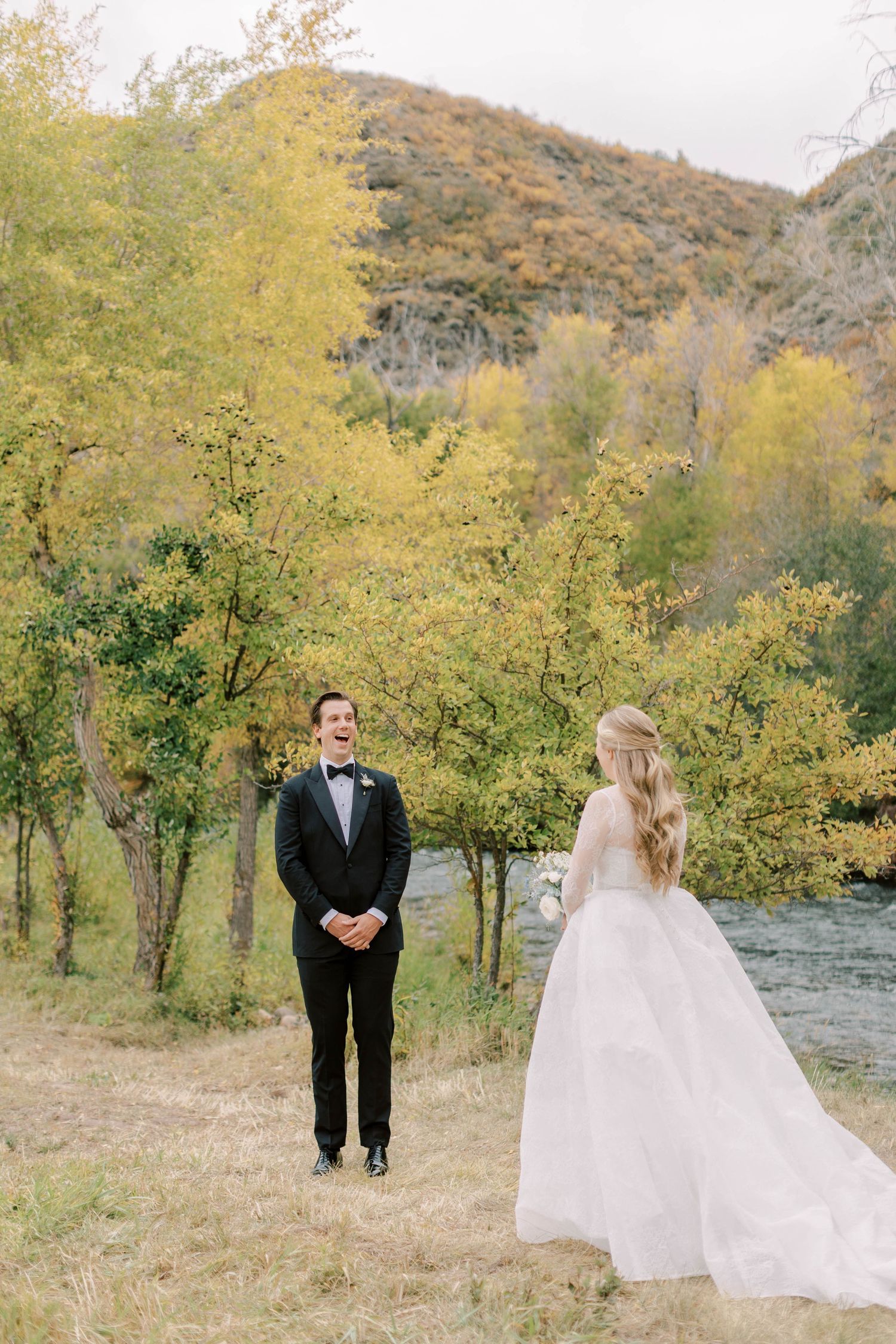 A couple shares a first look moment in a beautiful autumn mountain setting by a river.