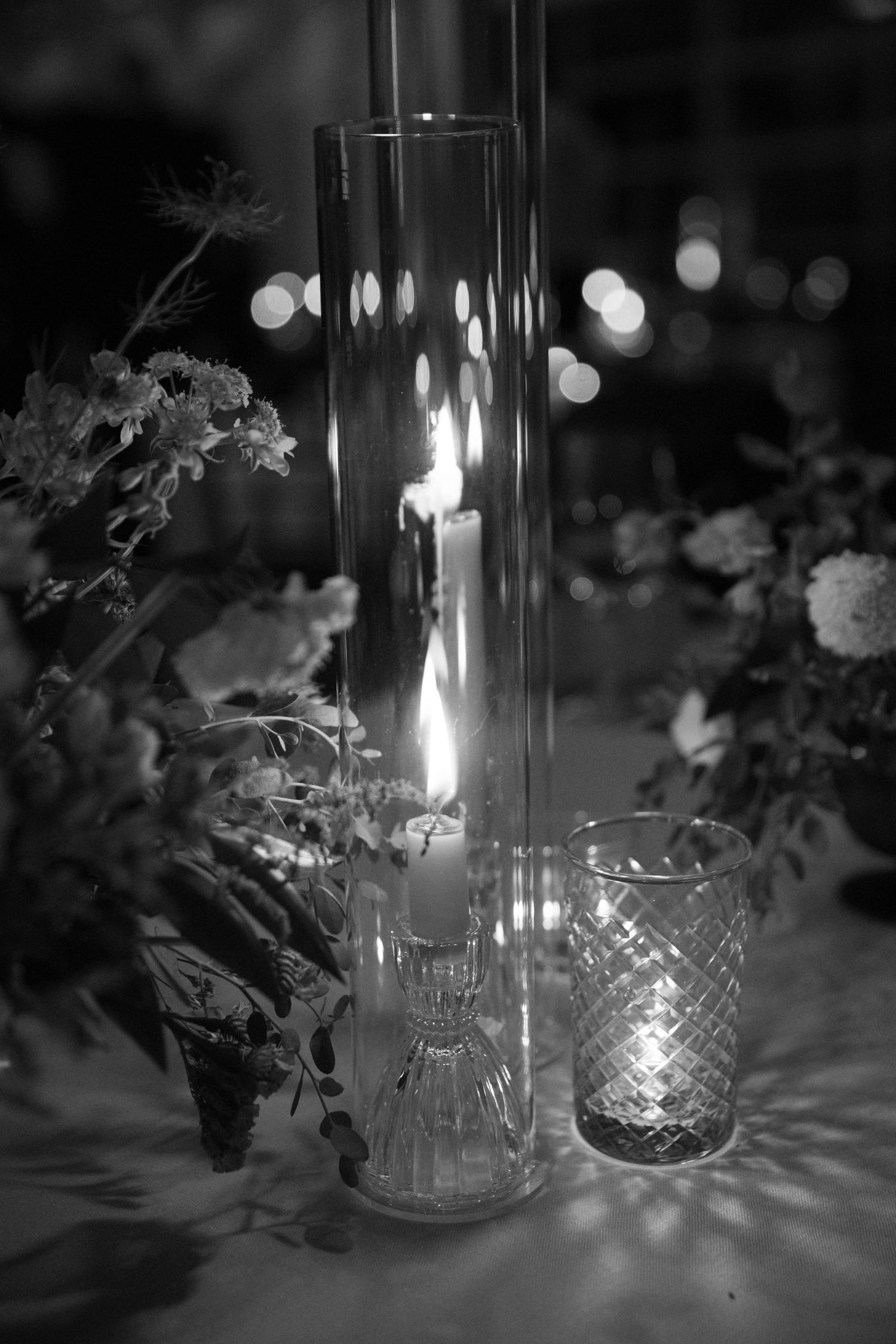 Elegant glass candleholders and vases with glowing lights create romantic ambiance at wedding reception.