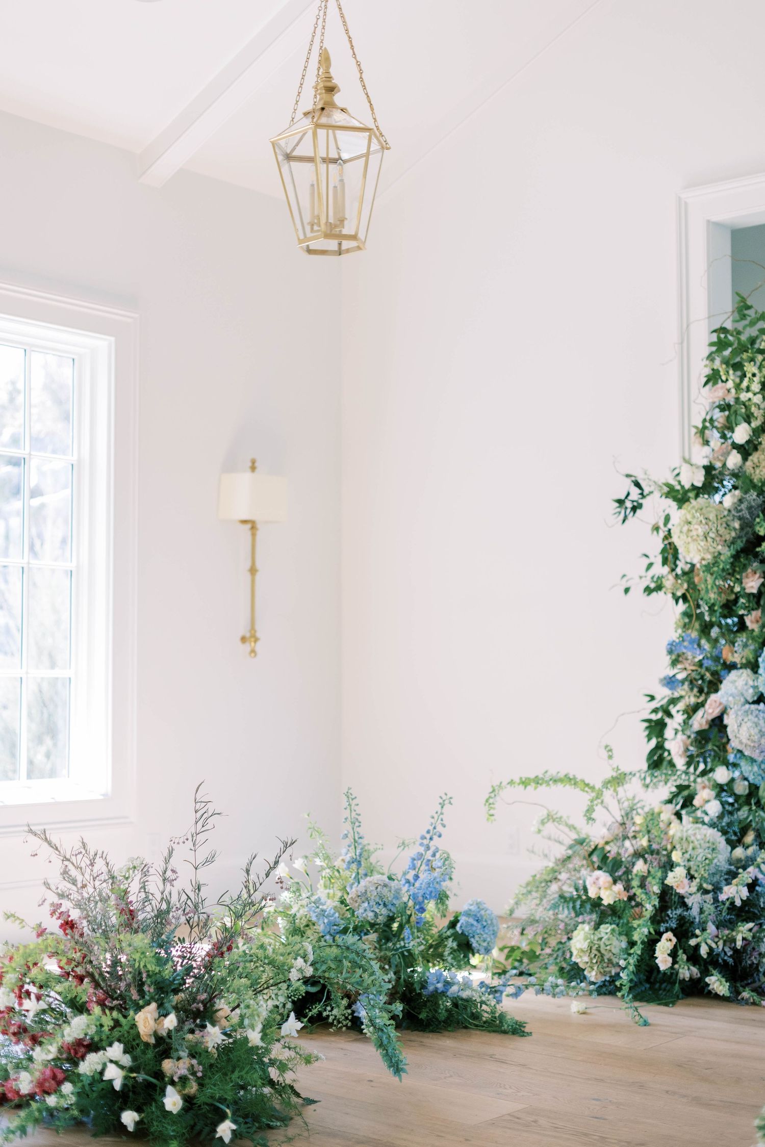 Gold lantern pendant lights hang above romantic floral arrangements in a bright white interior.