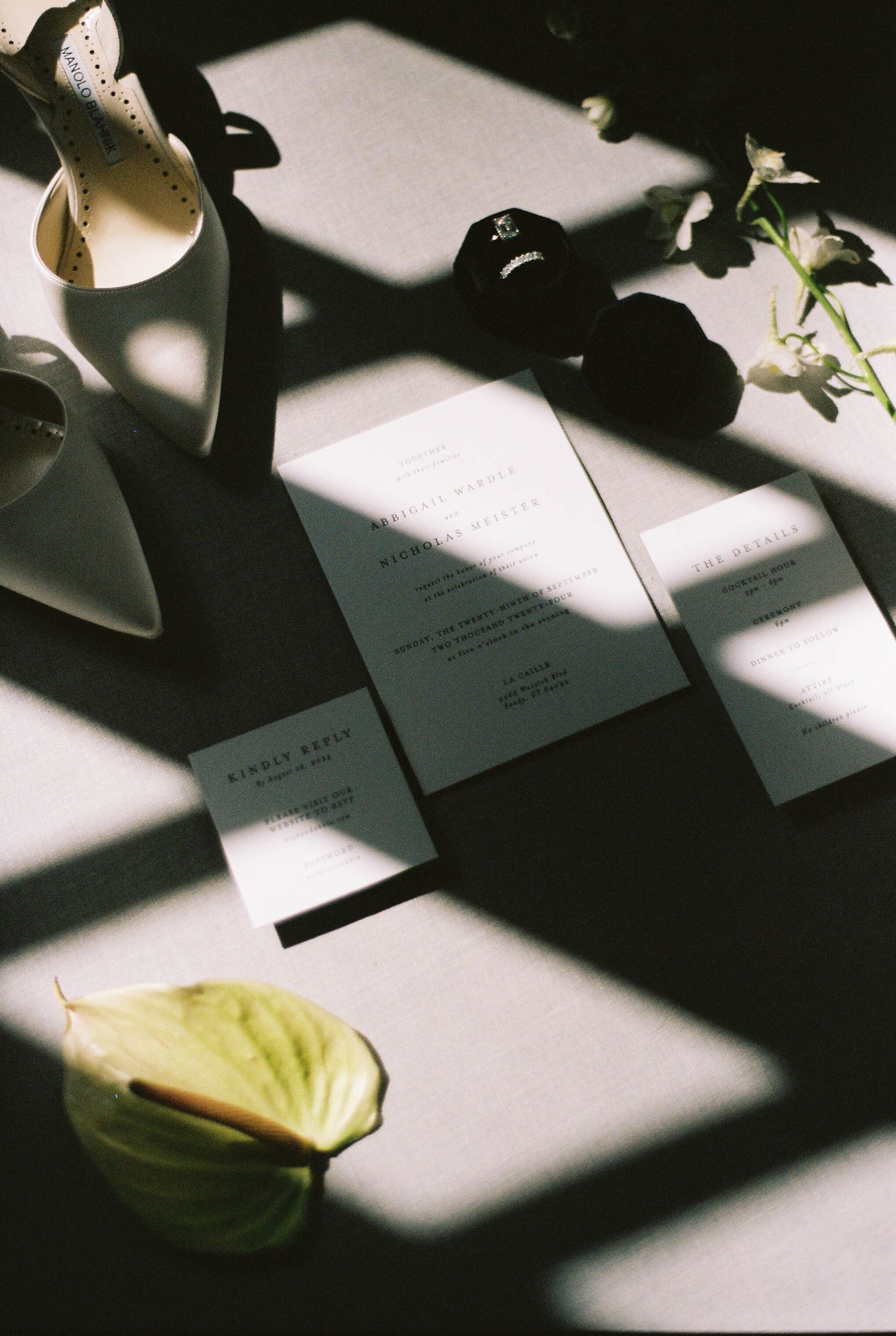 Wedding stationery and shoes creating artistic shadows on white surface.