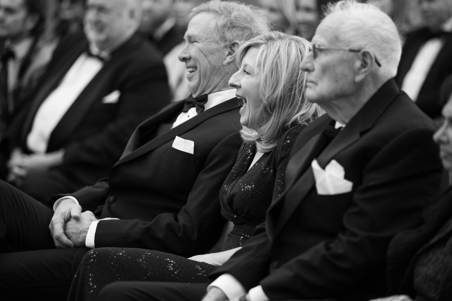Wedding guests laugh together during ceremony in black and white photograph.