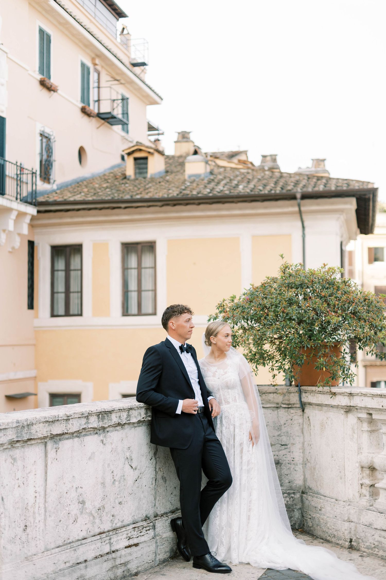 Newlywed couple poses elegantly against a beige building facade in Rome with classic Italian architecture.