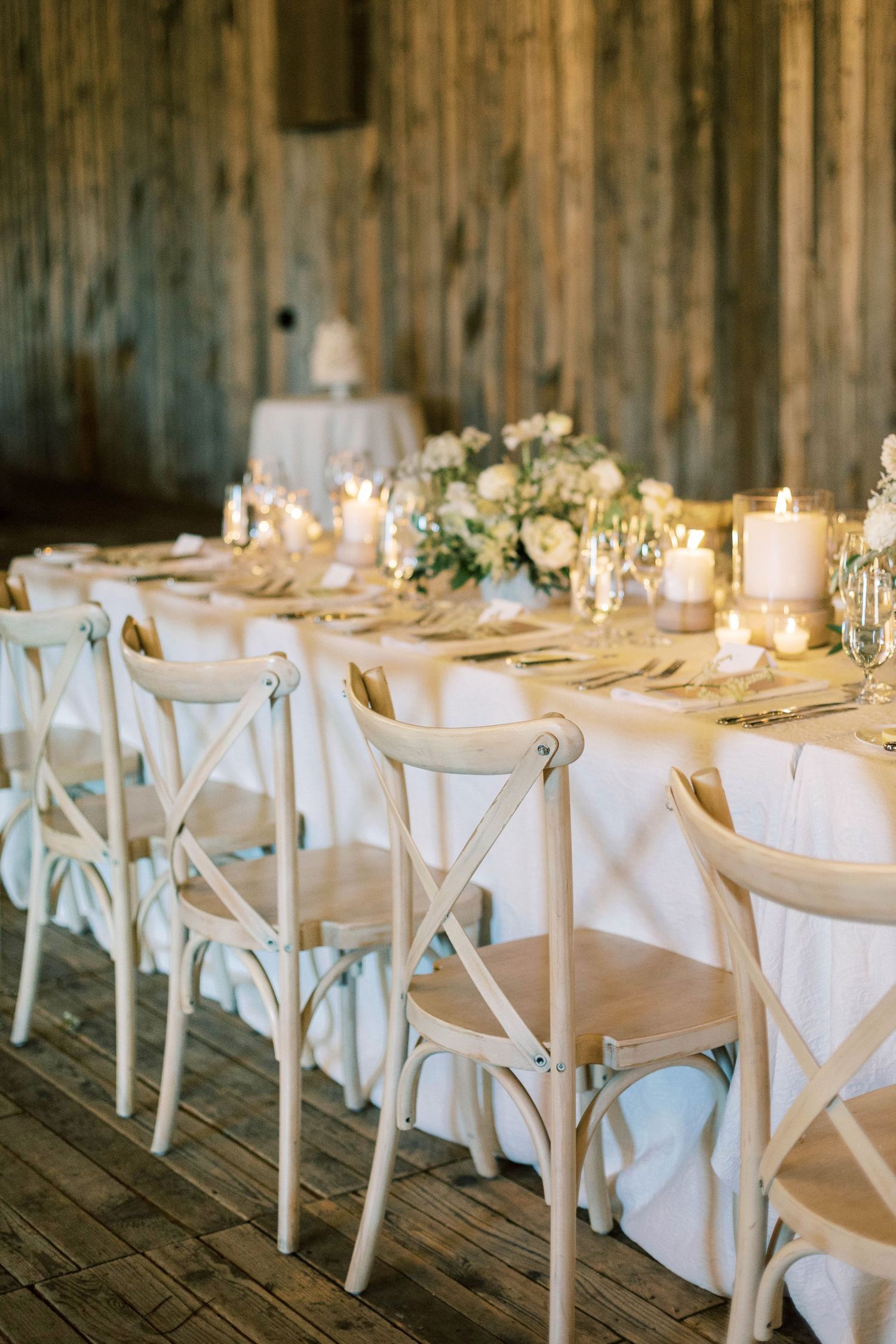 Elegant wedding table setting with white linens and cross-back chairs in rustic venue.