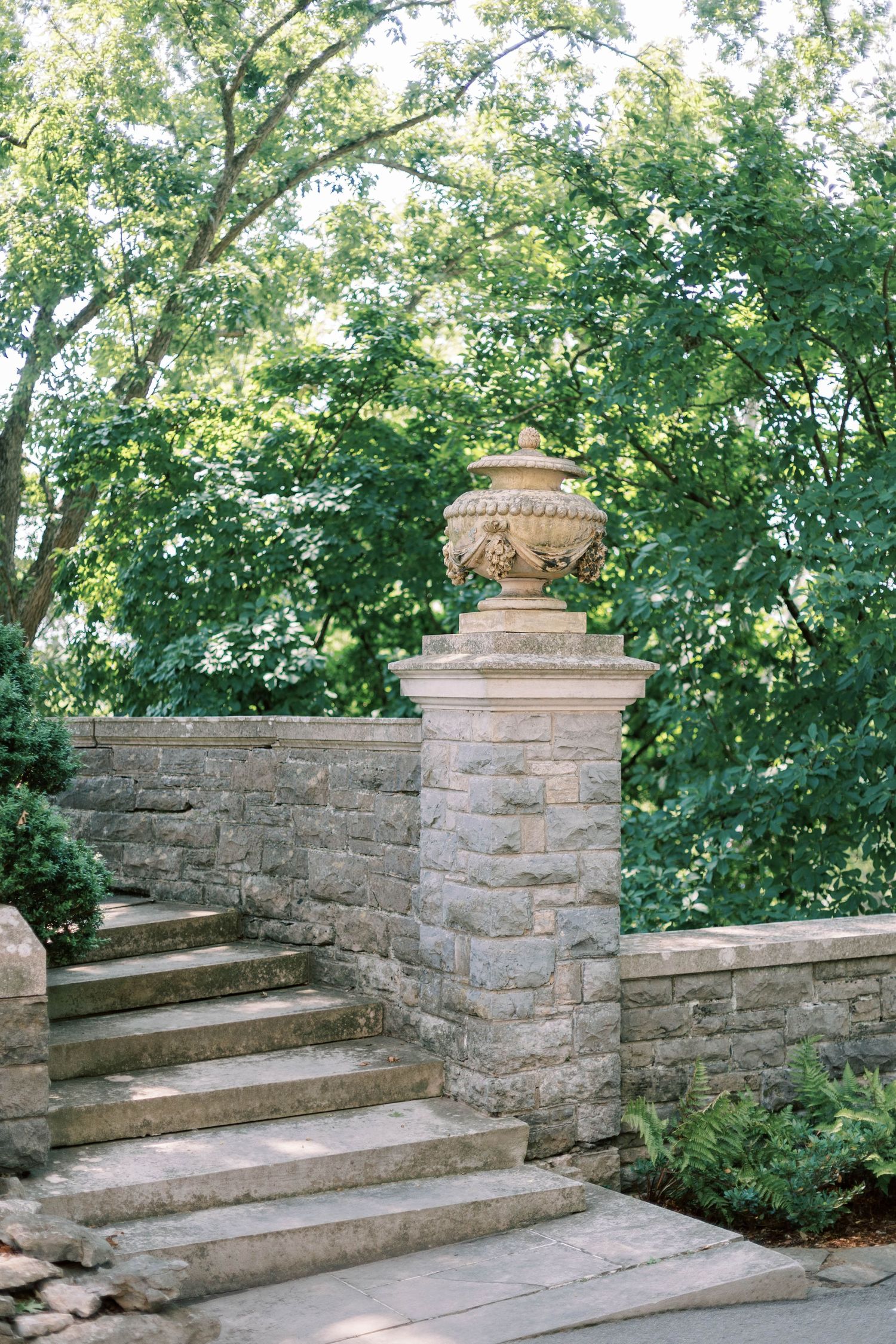 Stone garden steps with decorative urn pillar surrounded by lush summer greenery.