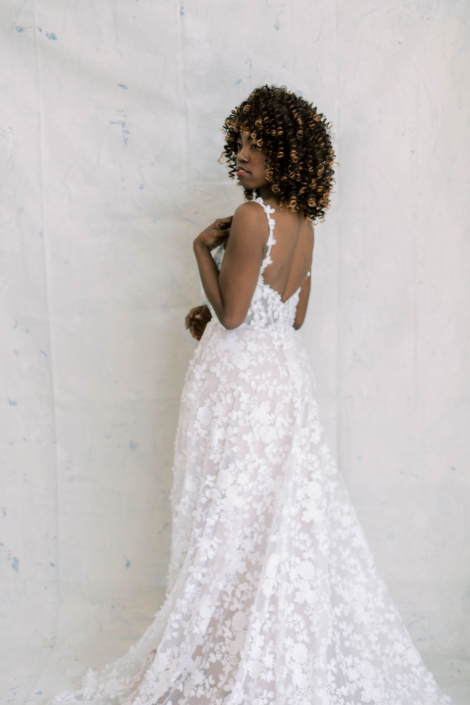 A white lace wedding gown with an open back design flows gracefully to the floor.