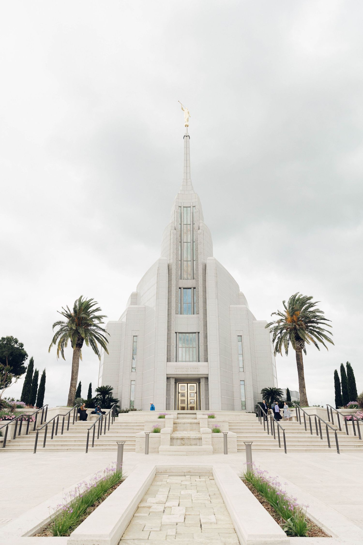 Majestic white Mormon temple with tall spire and palm trees against cloudy sky in architectural style of rome italy lds temple.