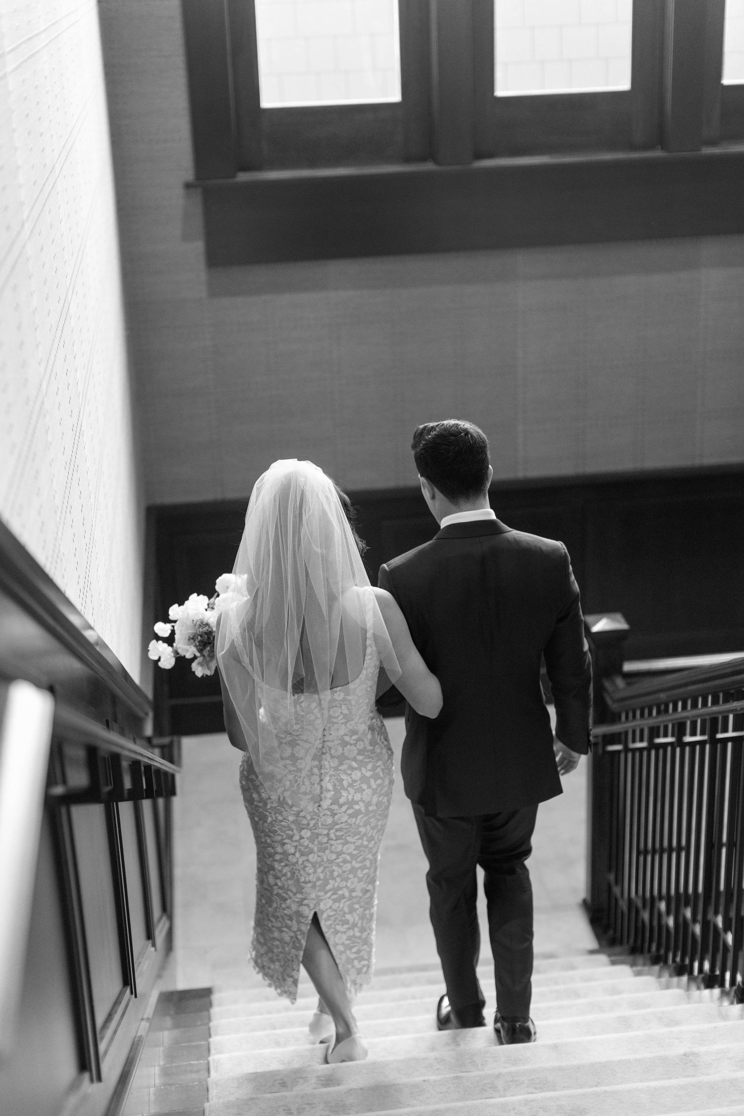 Black and white photo of newlyweds descending a staircase together after their ceremony.