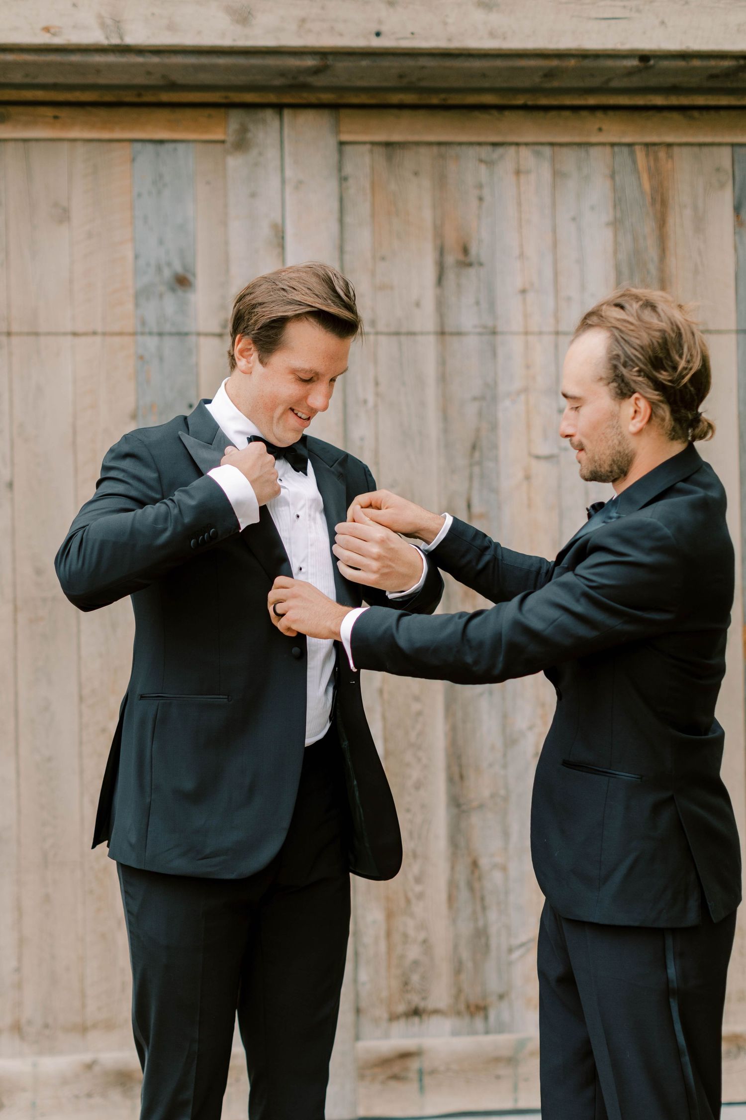 Groomsmen helping adjust each other's tuxedos before wedding ceremony.