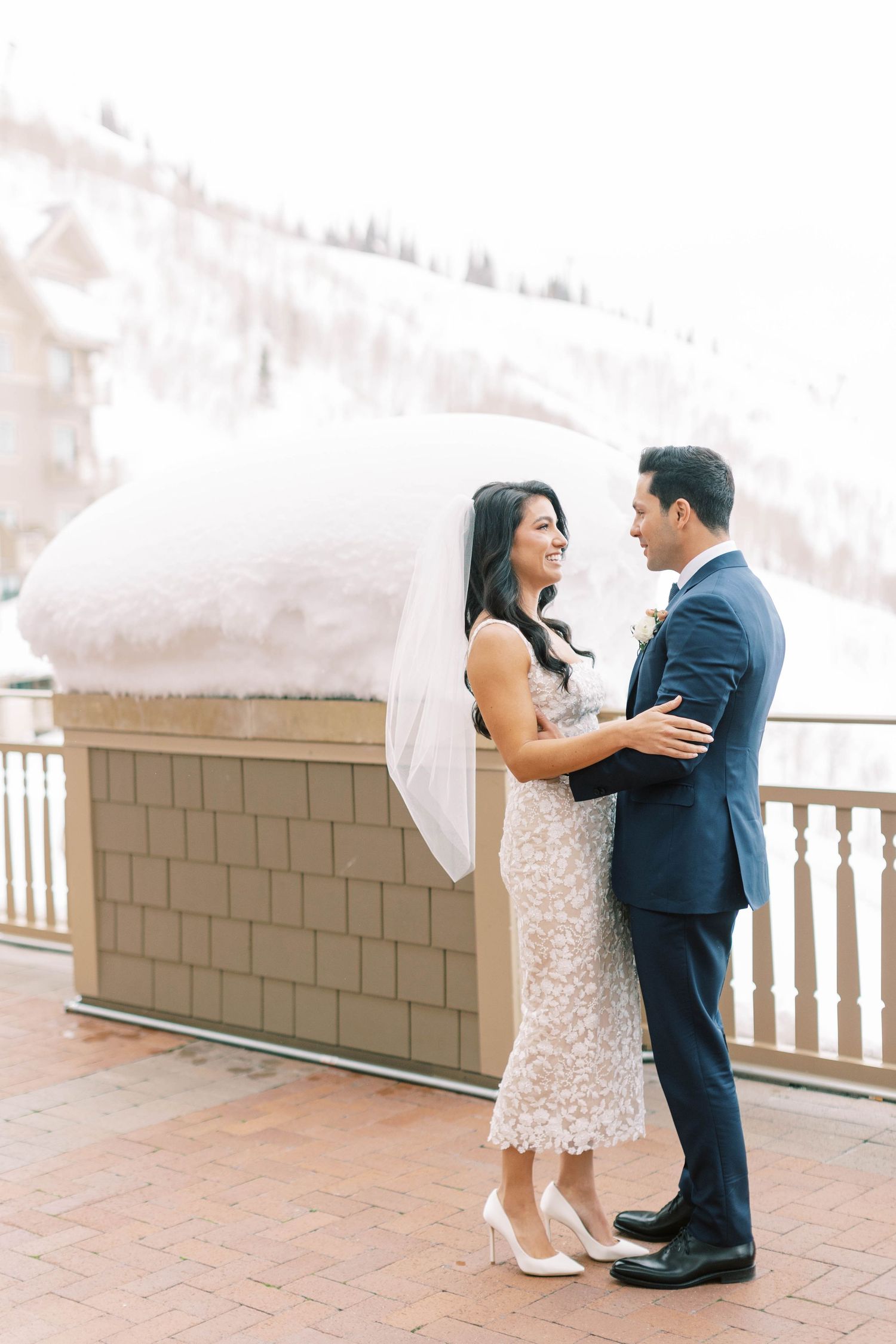 Romantic winter wedding moment on terrace with snow-capped mountains in background.