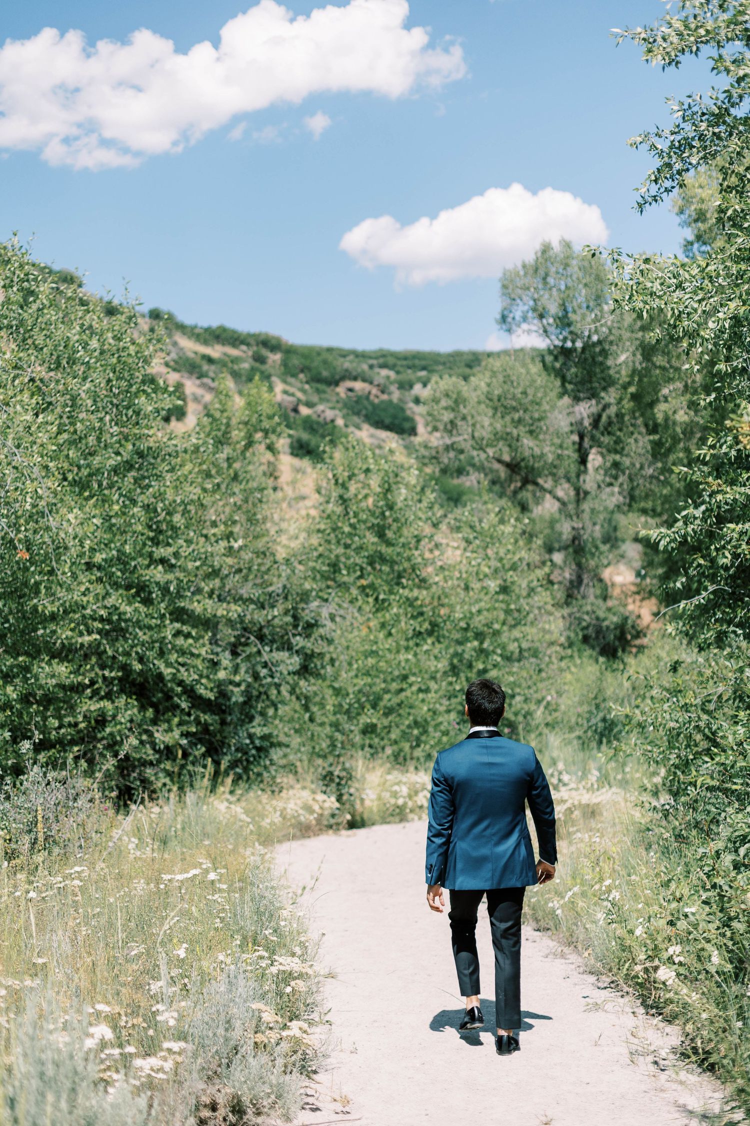 Person in a blue suit walking alone on a nature path surrounded by greenery.