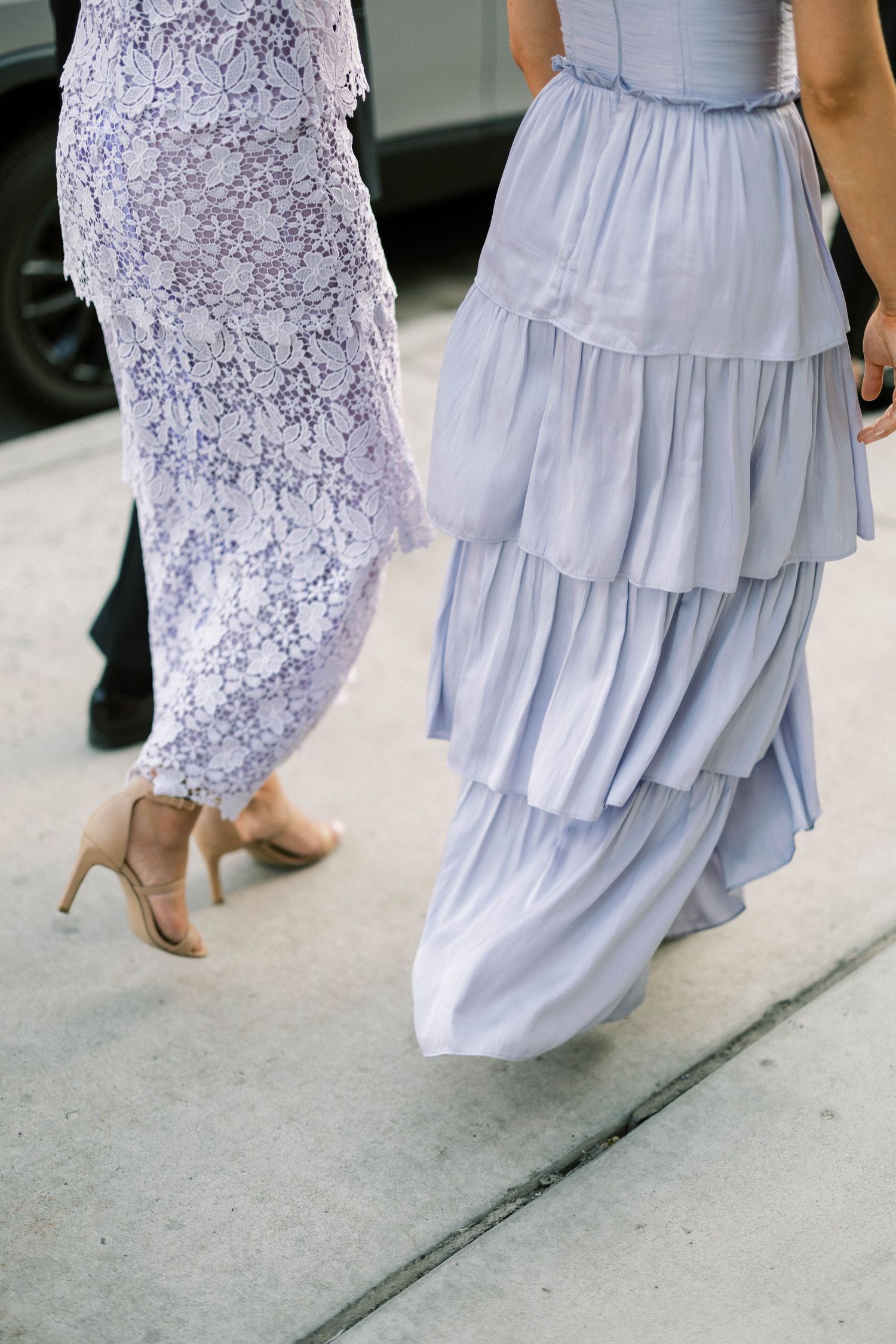 Close-up of bridesmaids' dresses in light blue and lilac with tiered skirts and ruffles.