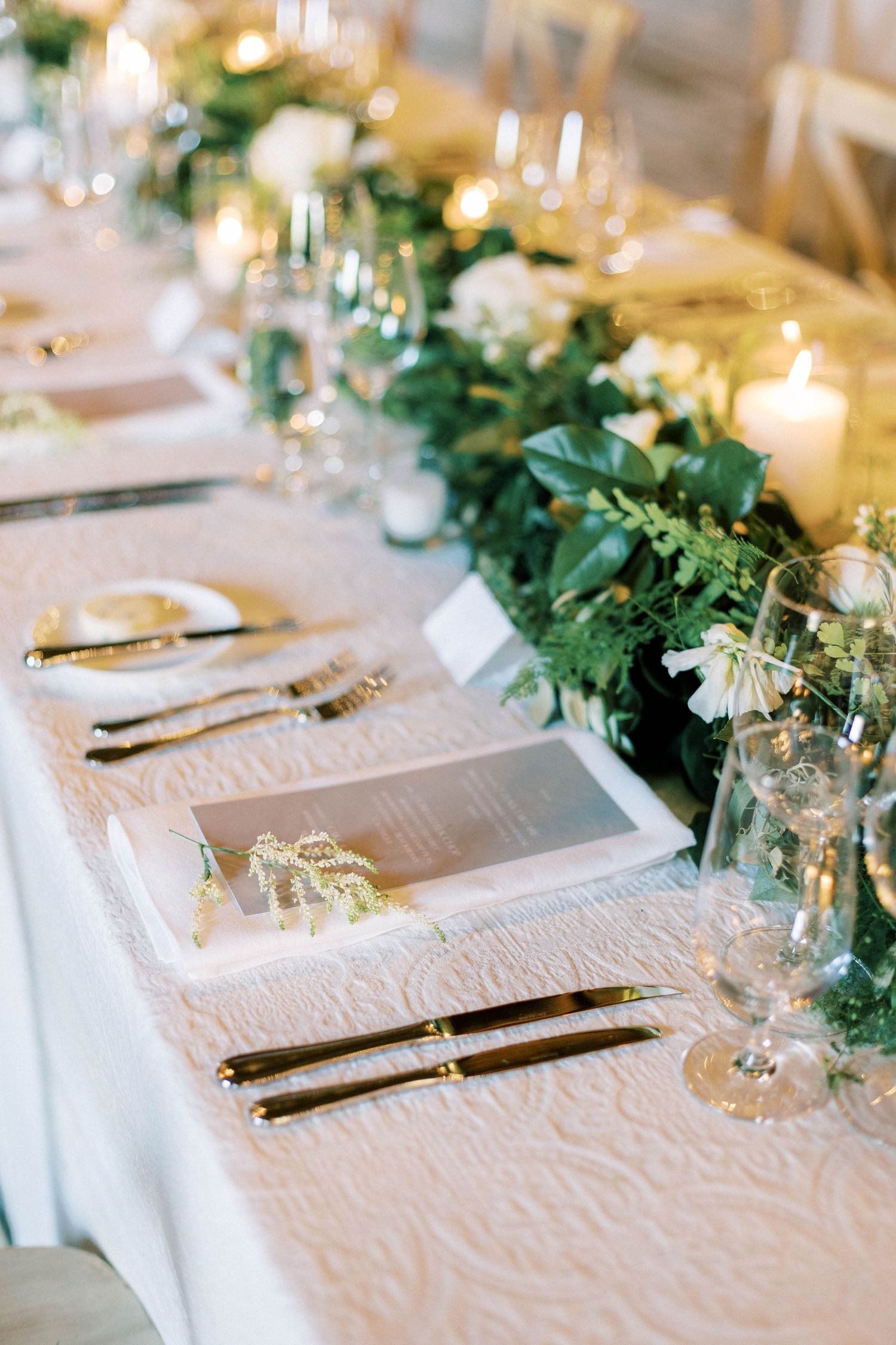 Elegant wedding table setting with white tablecloth and greenery centerpiece garland.