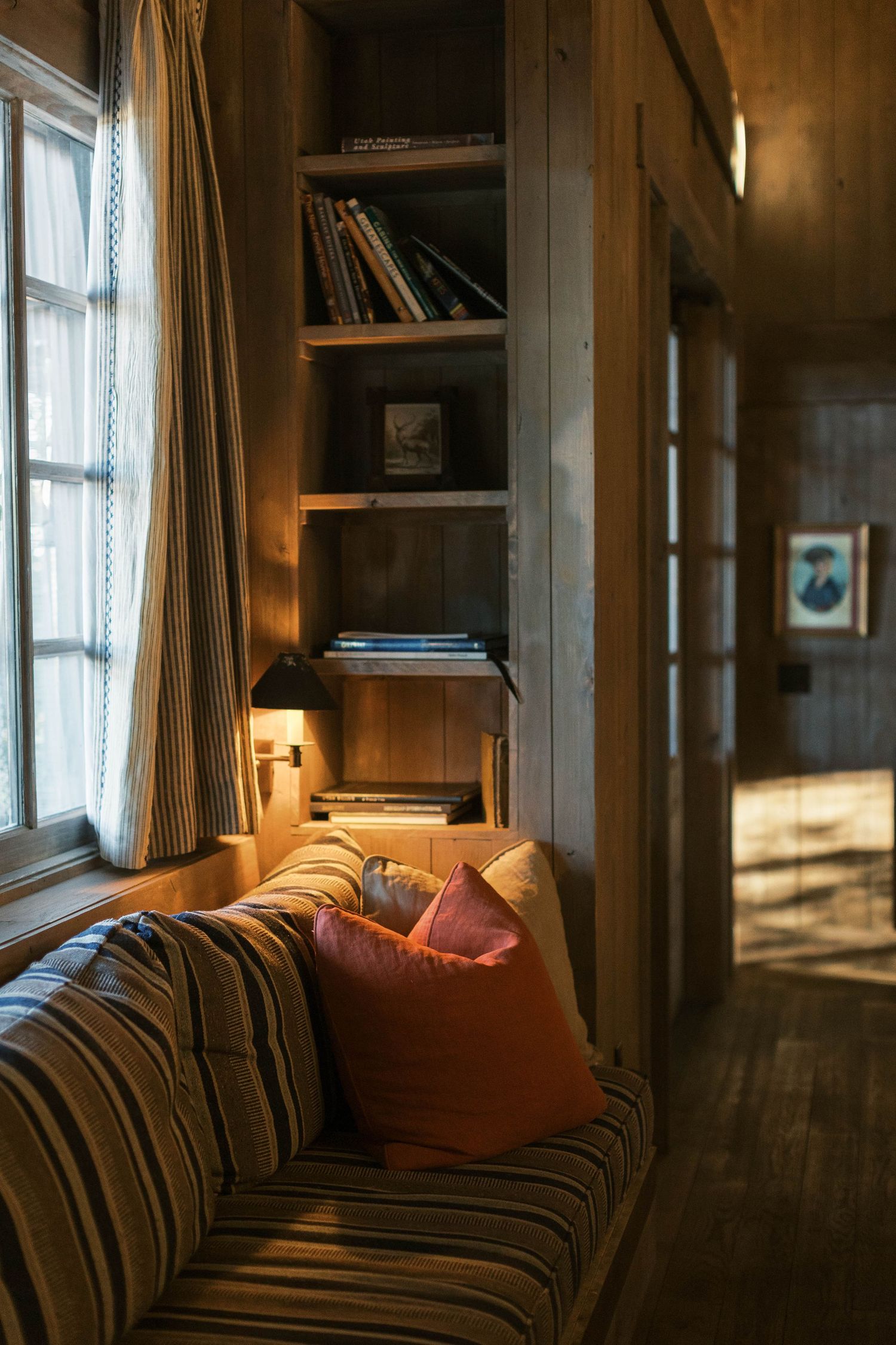 Cozy reading nook with built-in bookshelves, striped couch, and warm lighting by window.