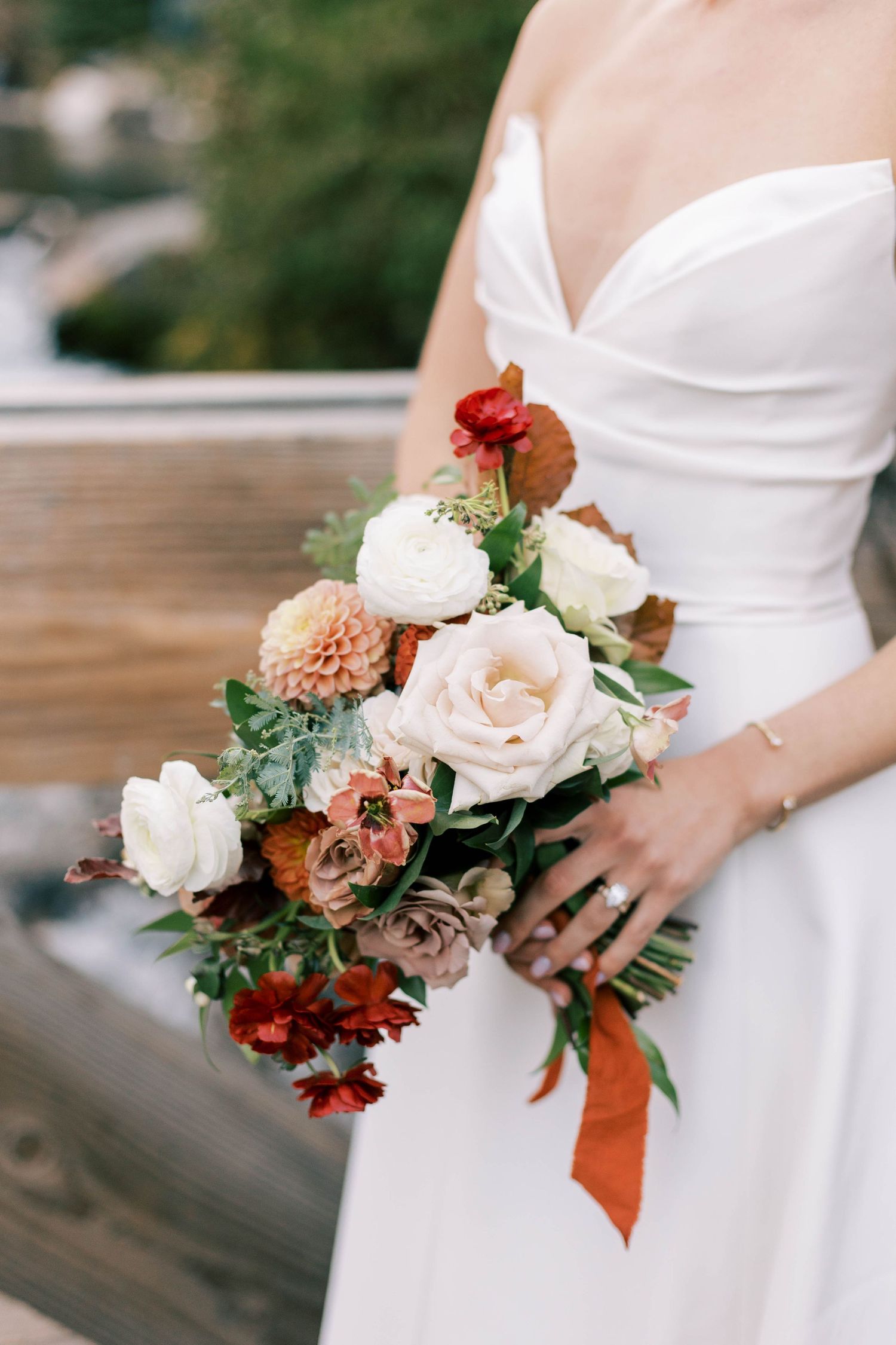 Close-up of bridal bouquet with white roses, coral dahlias and autumn-colored flowers.
