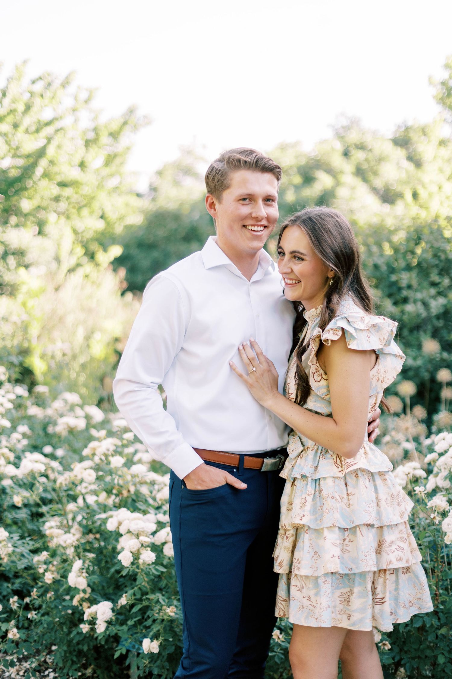 A couple poses together in a flowering Red Butte garden wearing coordinated spring outfits.