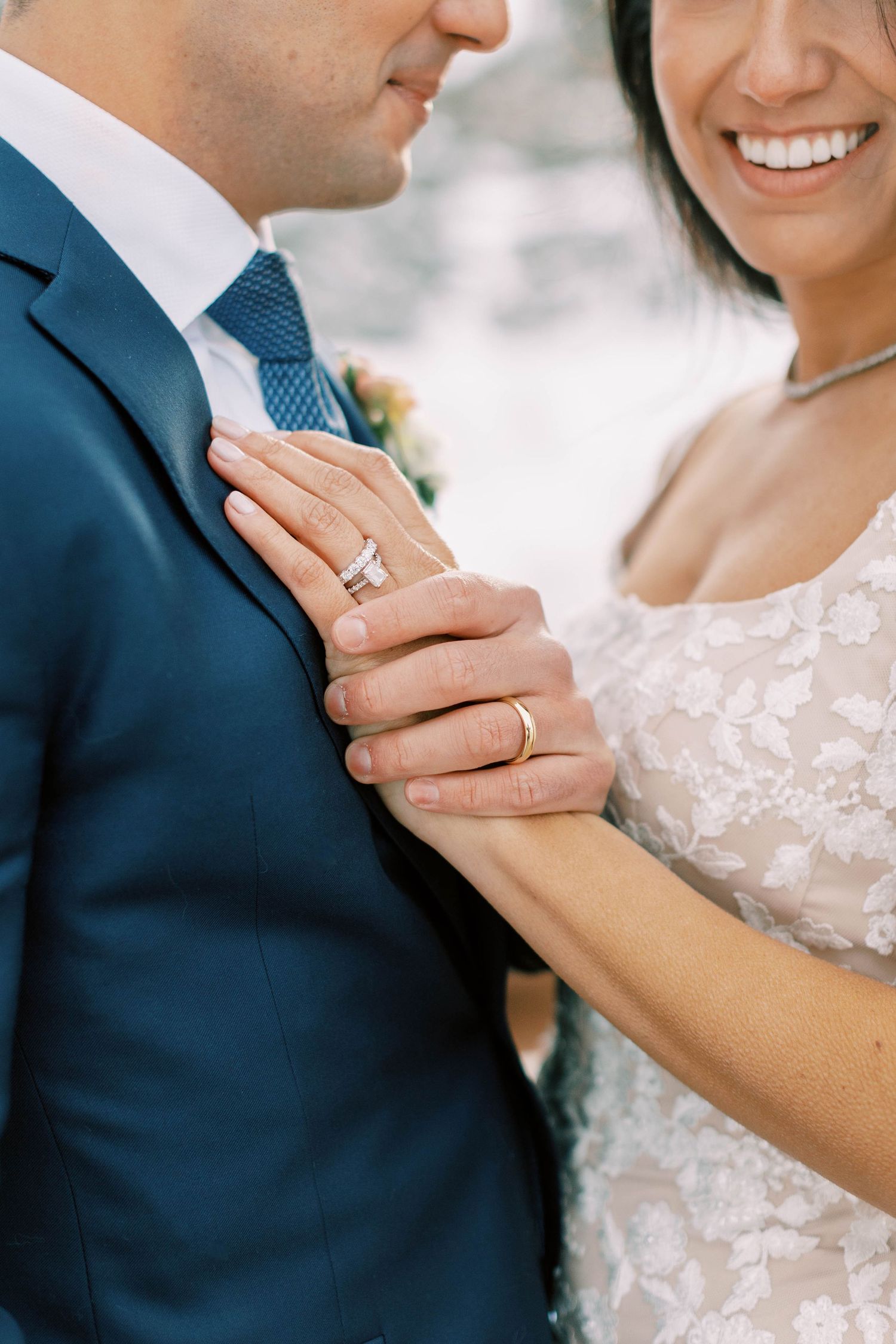 Close-up of wedding rings and hands against formal attire.