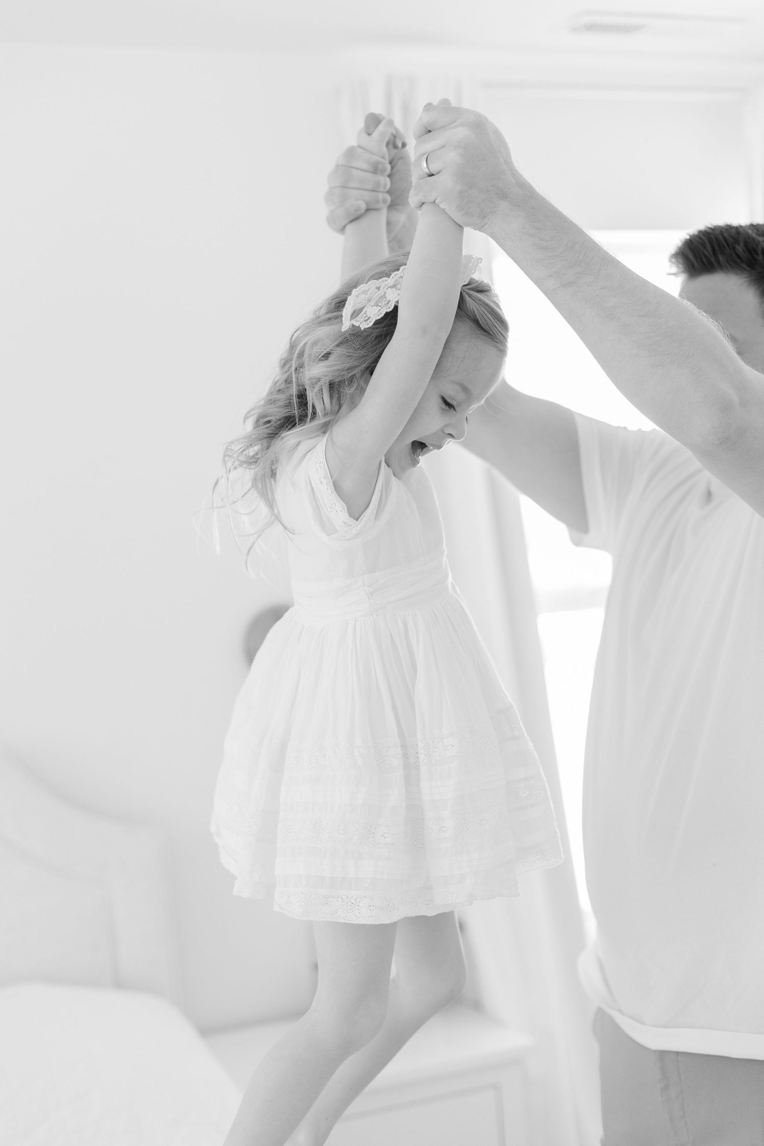 Parent and child in white clothing dancing and playing together against a bright background.
