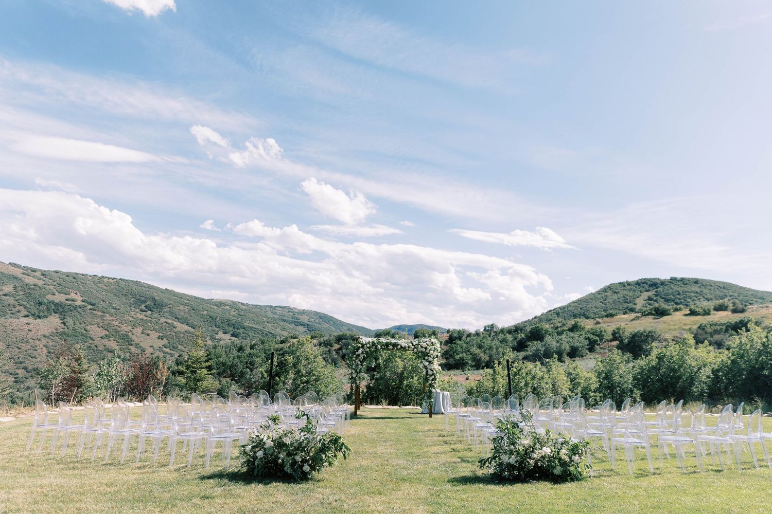 Scenic mountain wedding venue with rows of white chairs set up on grassy field.