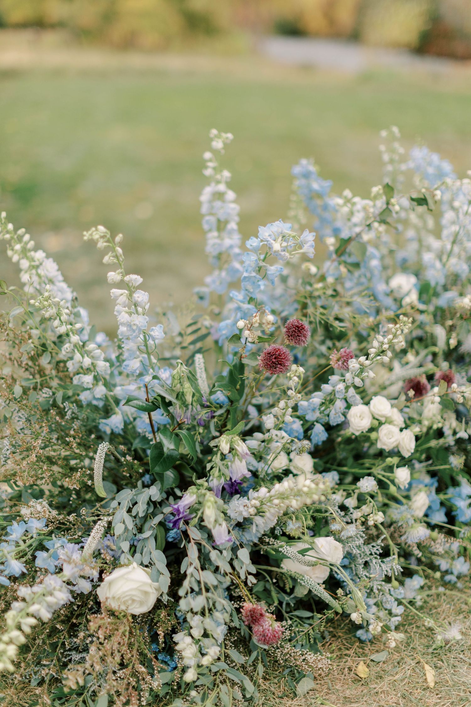 A lush garden-style floral arrangement with white, blue, and pink blooms against a natural backdrop.