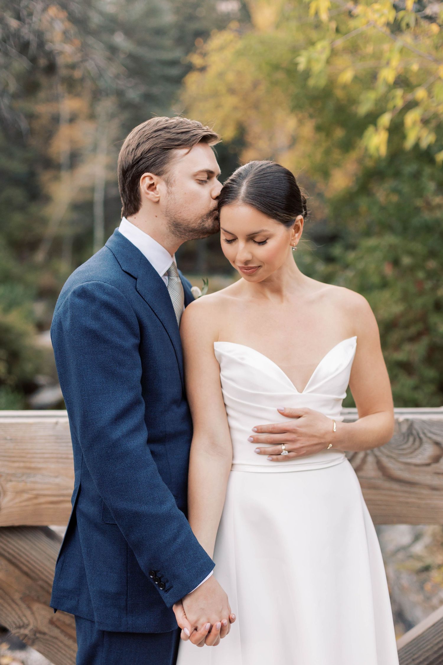 Intimate wedding moment captured on wooden deck with autumn foliage in background.
