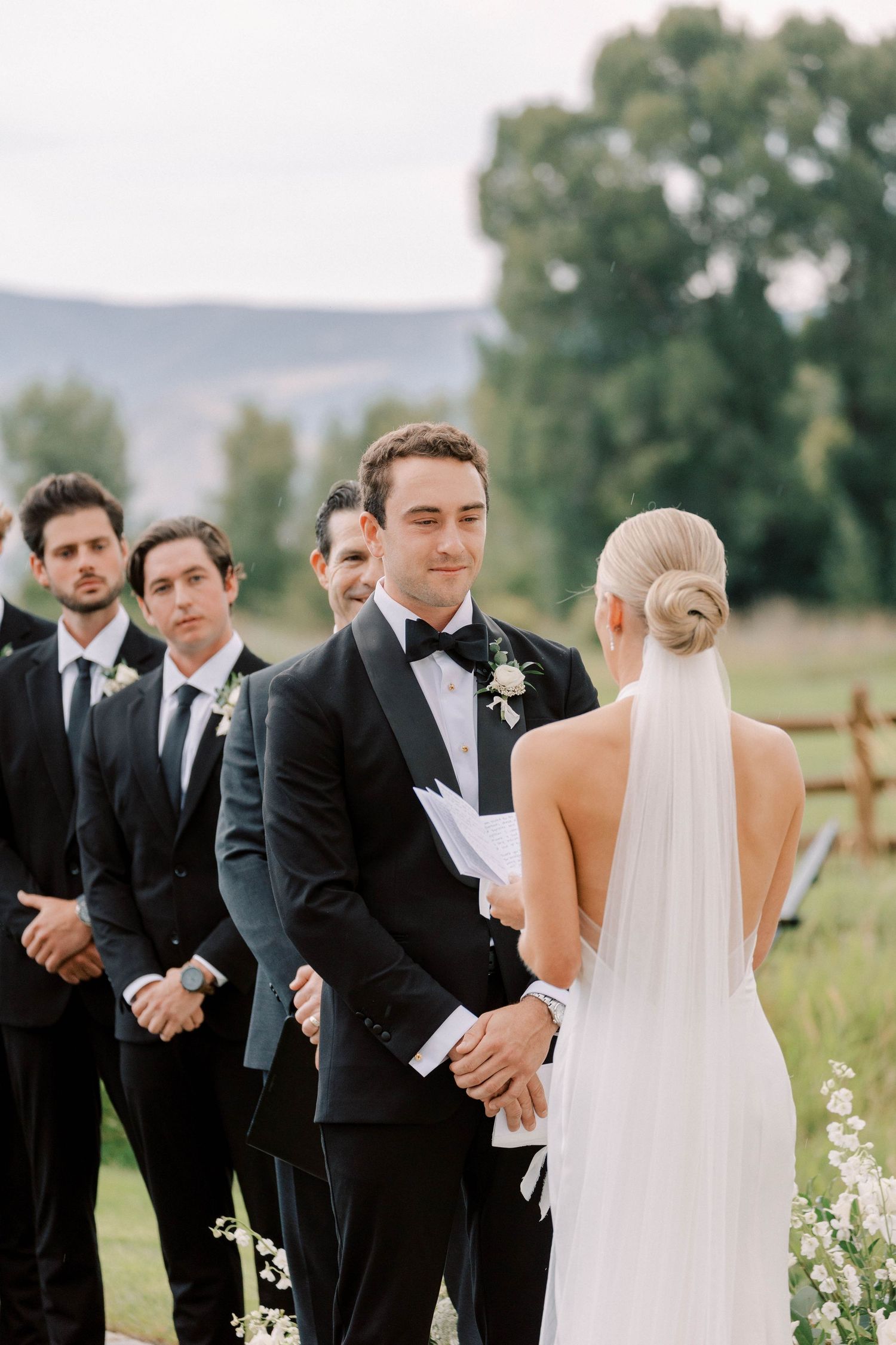 Intimate wedding ceremony moment with couple exchanging vows surrounded by groomsmen in dark suits.