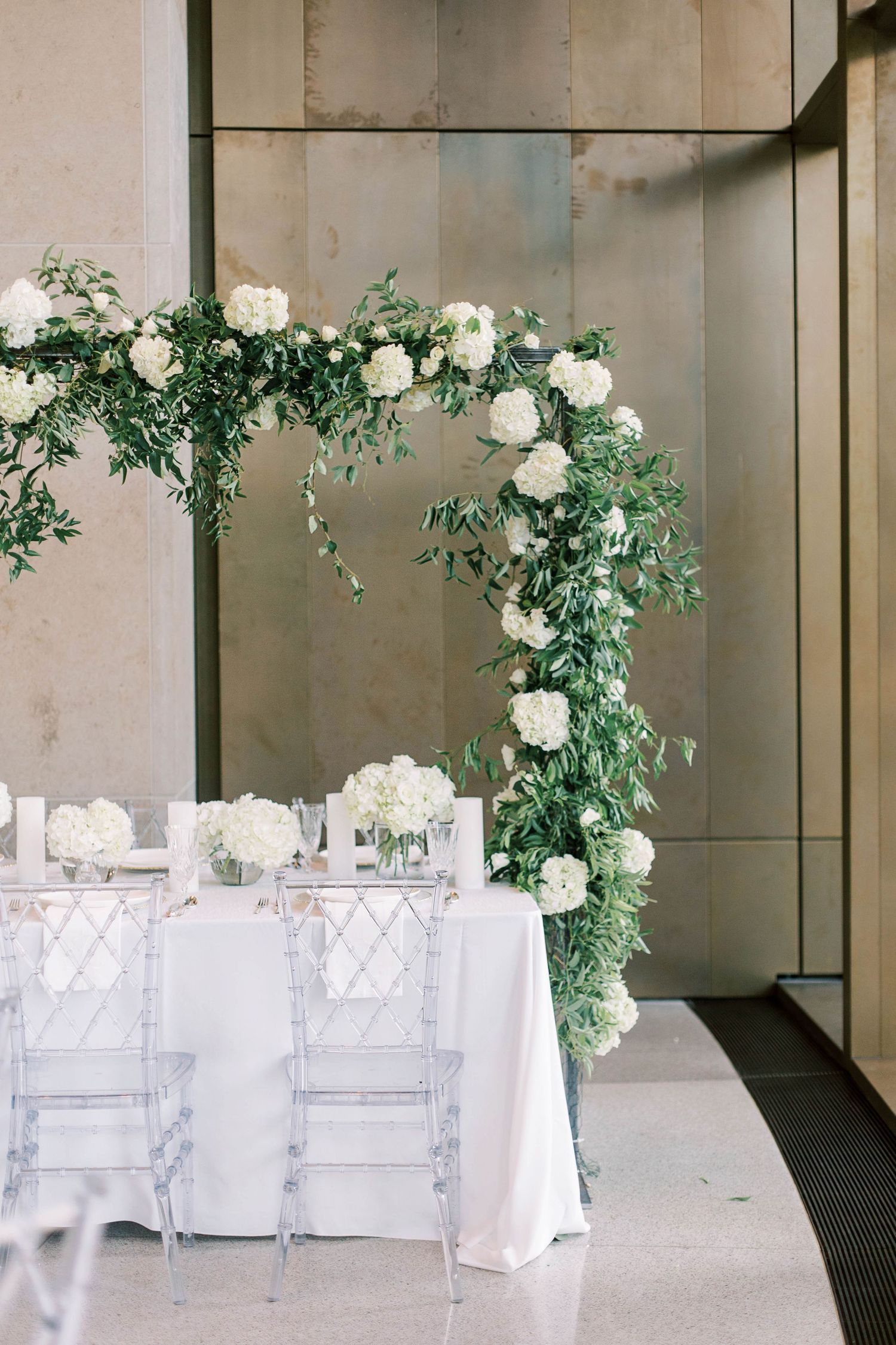 Modern wedding reception table with white floral arch and lucite chairs.