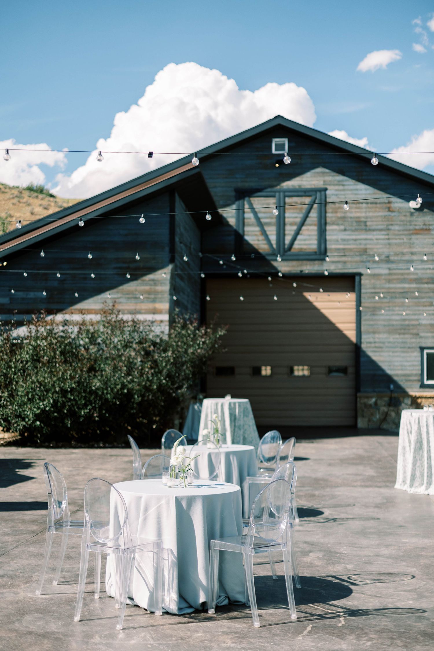 Modern barn venue with string lights and ghost chairs set for wedding reception.
