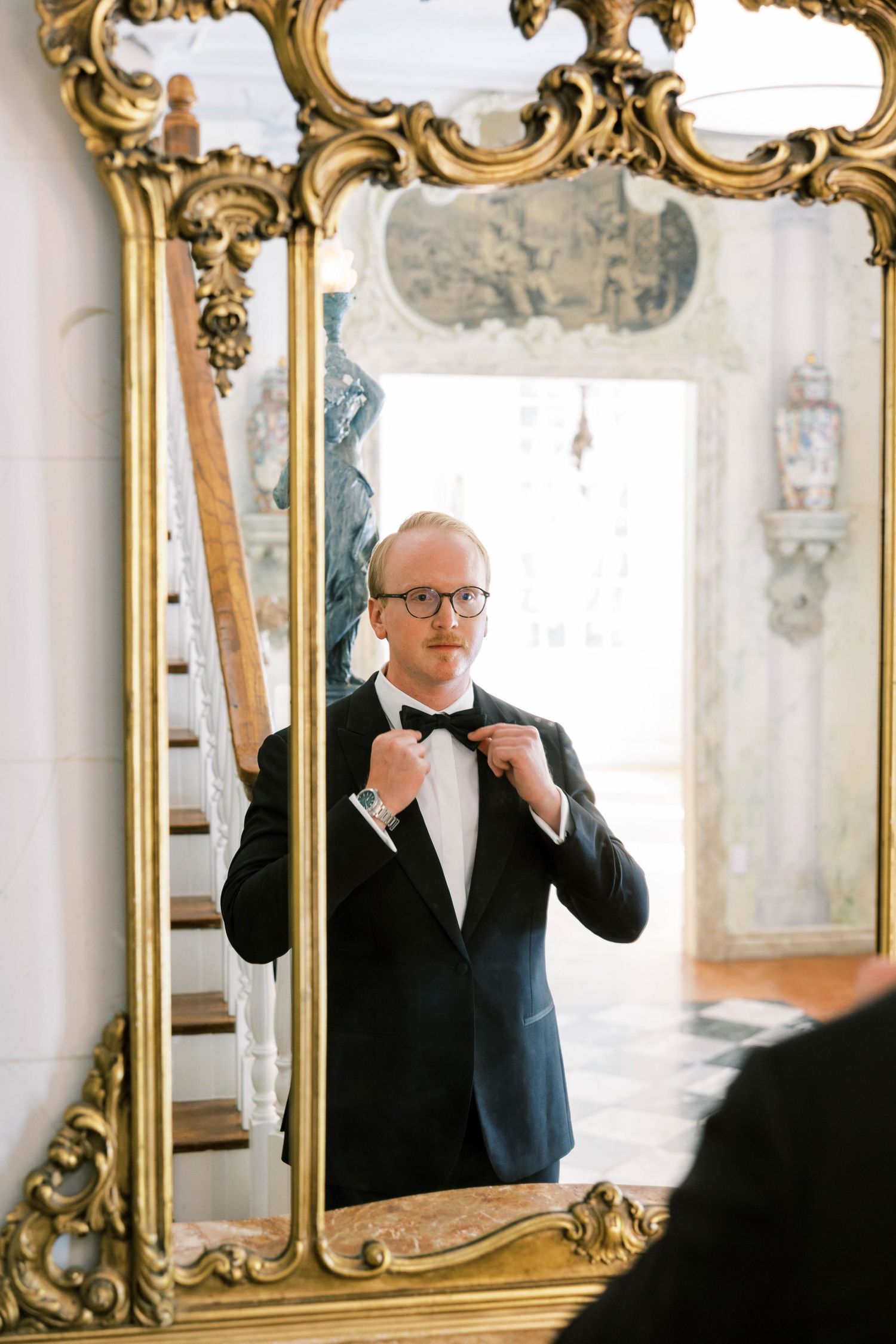 Reflection in ornate gold mirror shows formal attire preparation before event.