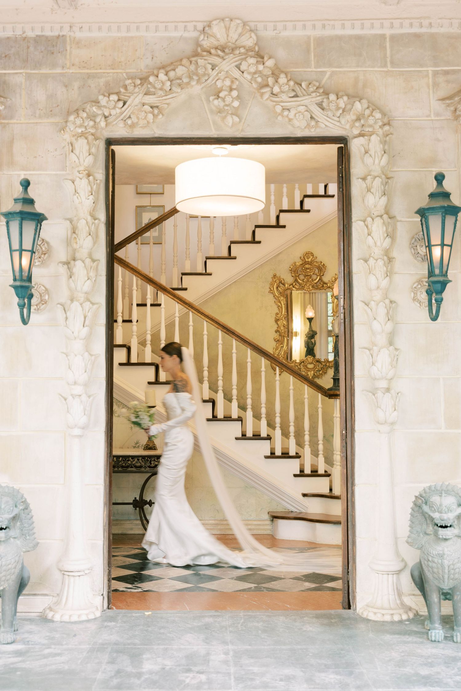 Wedding dress with long train framed by ornate doorway leading to grand staircase with turquoise lanterns.