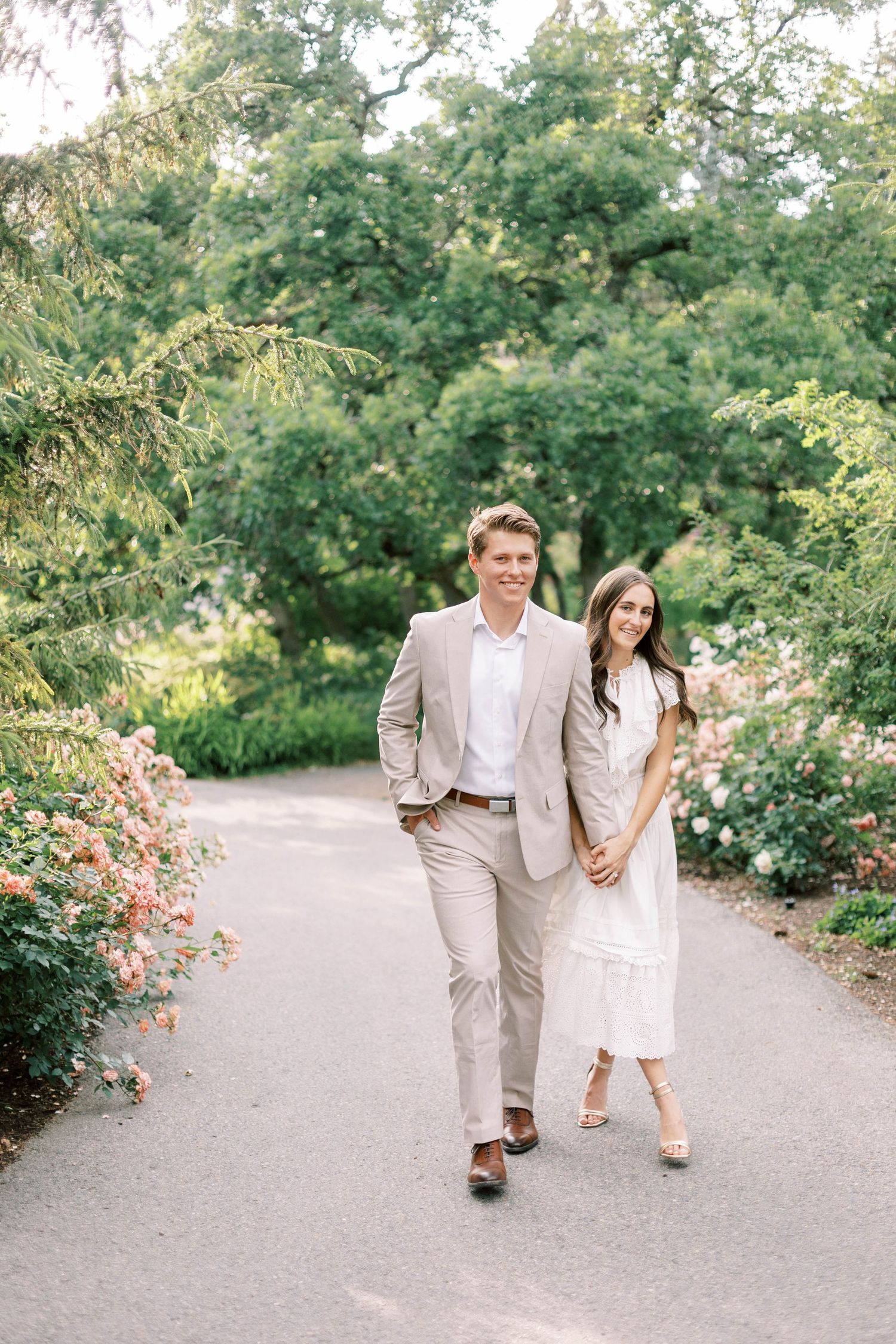 A couple walks hand in hand down Red Butte garden path wearing light colored formal attire.