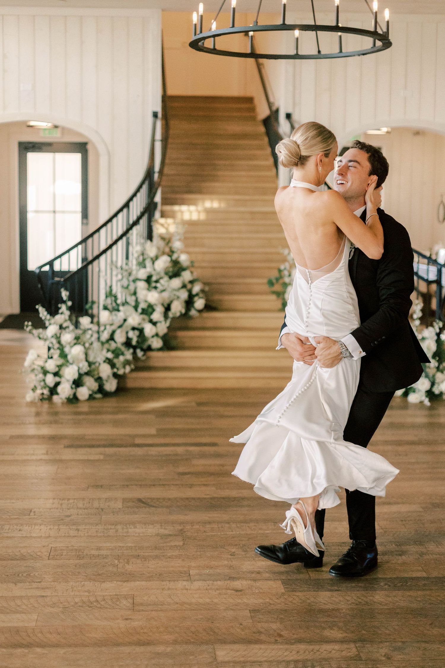 A couple sharing a joyful dance moment in an elegant venue with floral decorations.