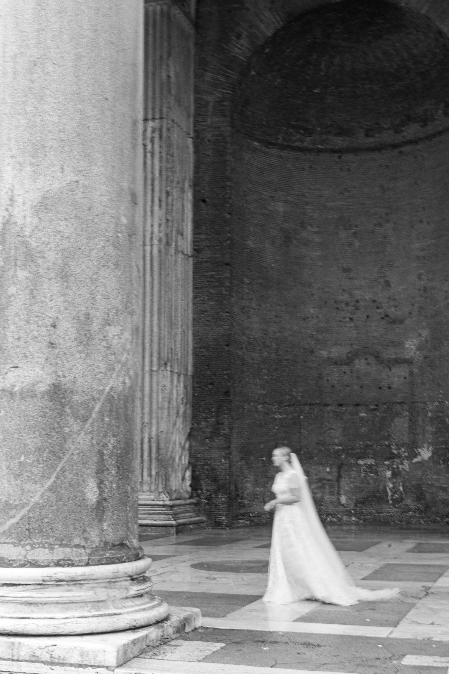 Black and white photograph of bride walking through the Pantheon's ancient Roman interior.
