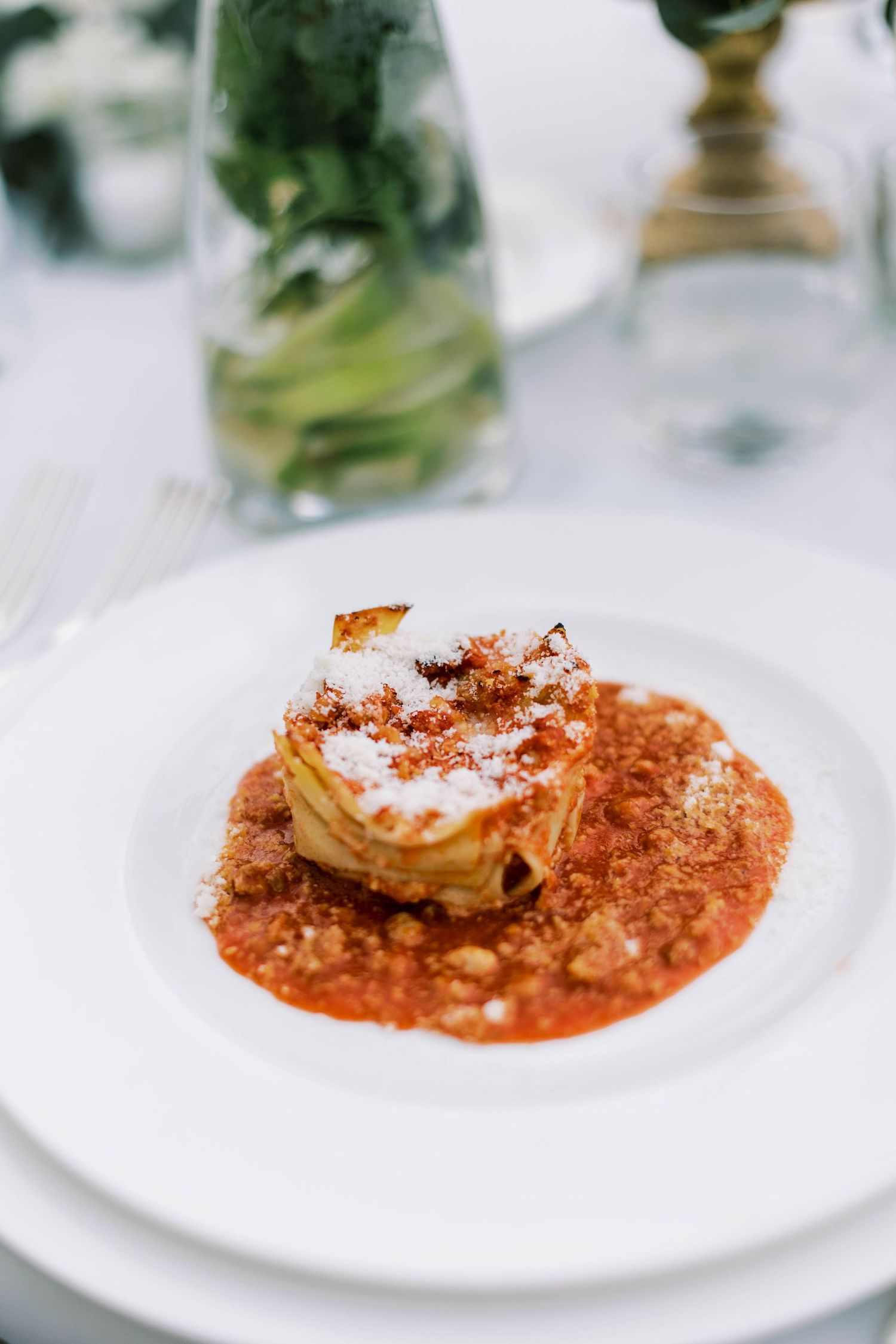 Artfully plated pasta dish with red sauce and garnish on elegant white plate in fine dining setting.
