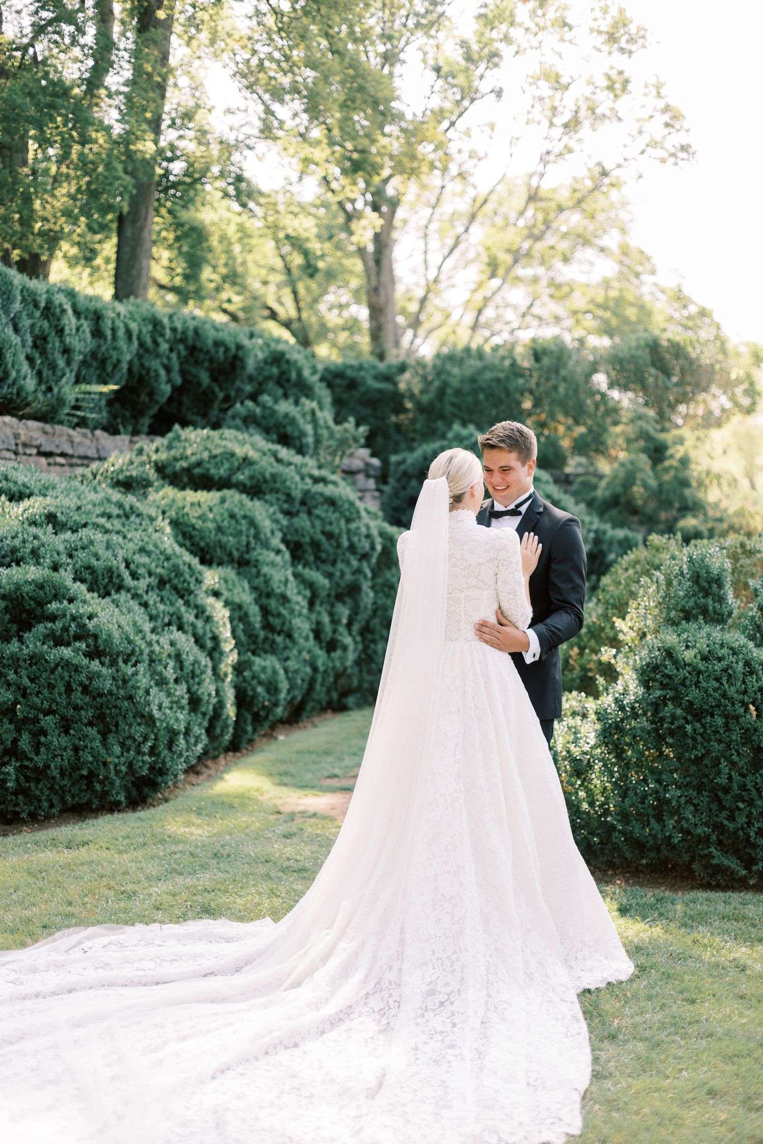 Elegant wedding portrait in a garden setting with flowing white dress and manicured hedges.
